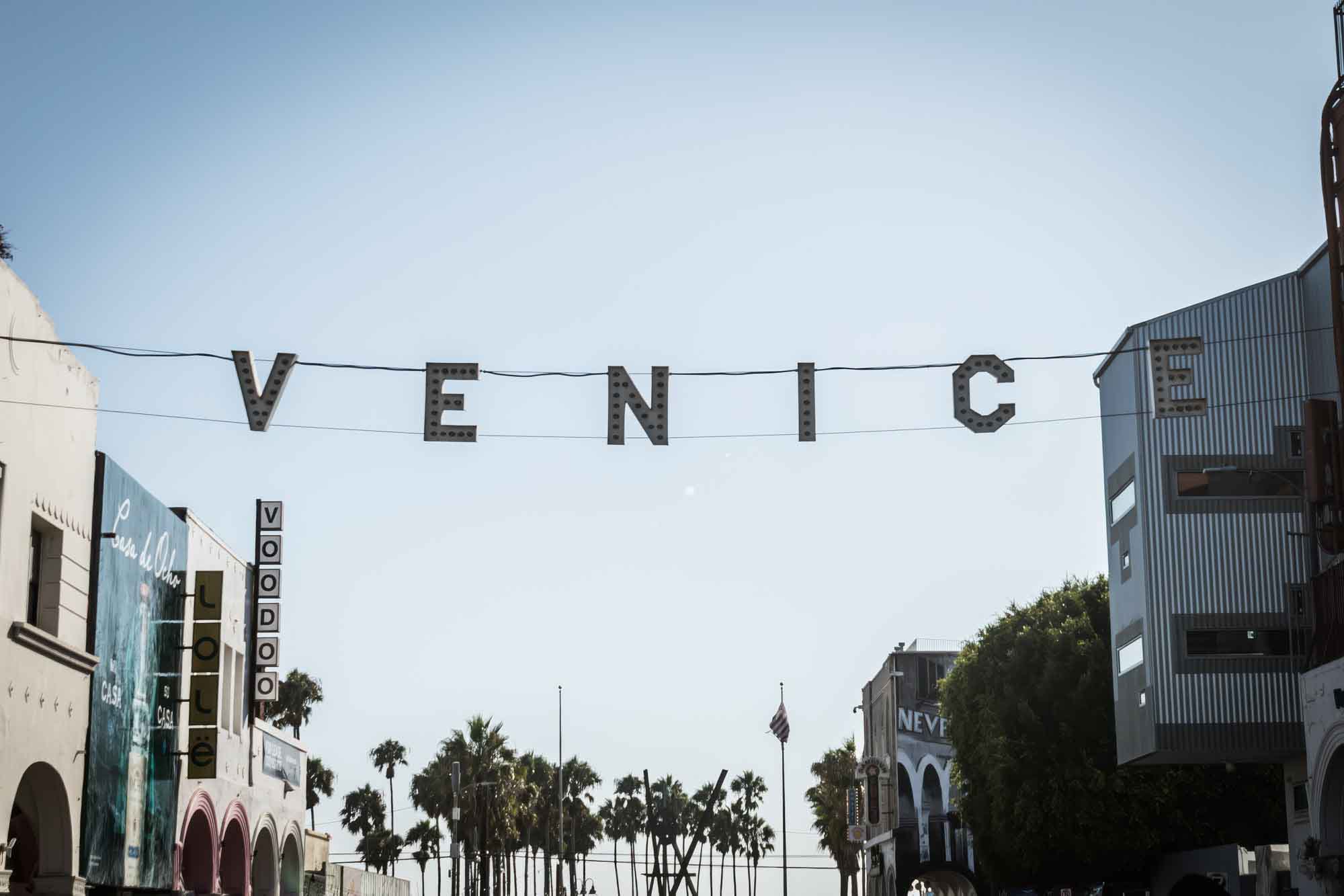 The iconic Venice sign in front of buildings and palm trees for an article on Venice Canals engagement photos