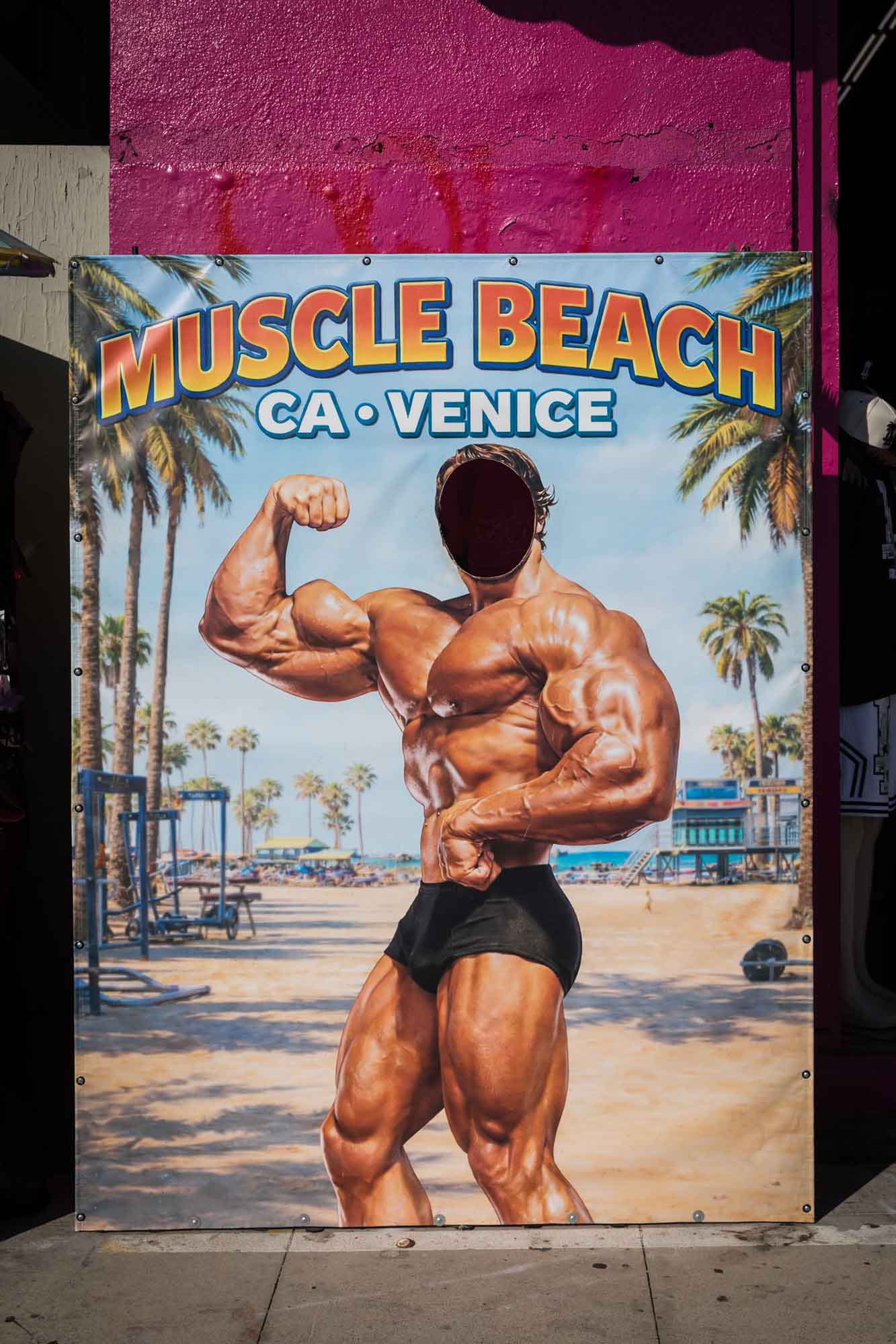 Wooden poster of Arnold Schwarzenegger with cut out face and sign that says Muscle Beach CA Venice for an article on Venice Canals engagement photos