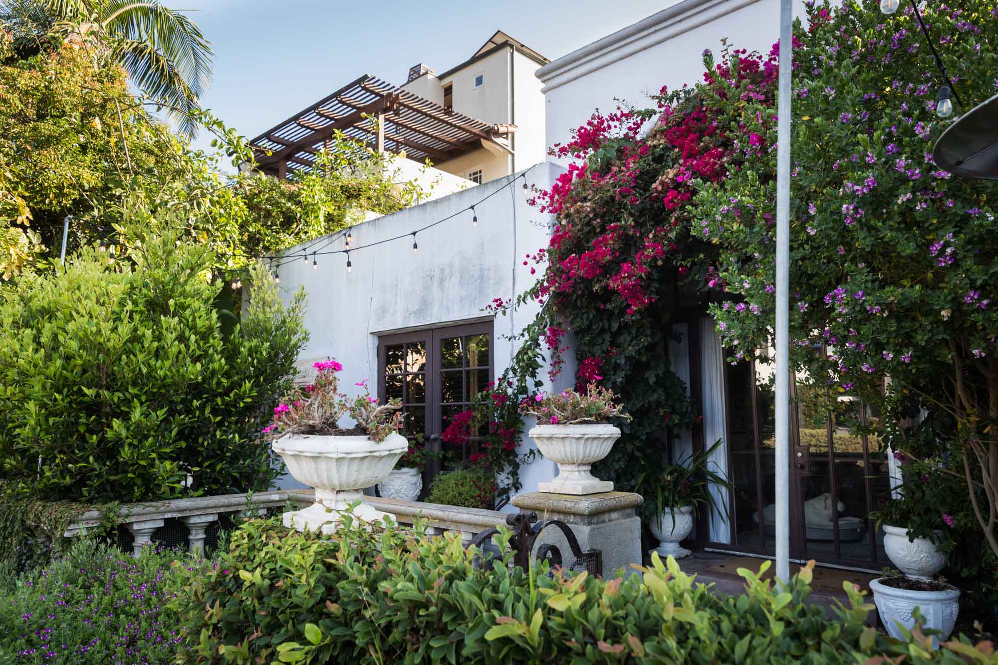 Concrete home surrounded by colorful flowers and two white urns filled with flowers with a pergola on the roof for an article on Venice Canals engagement photos