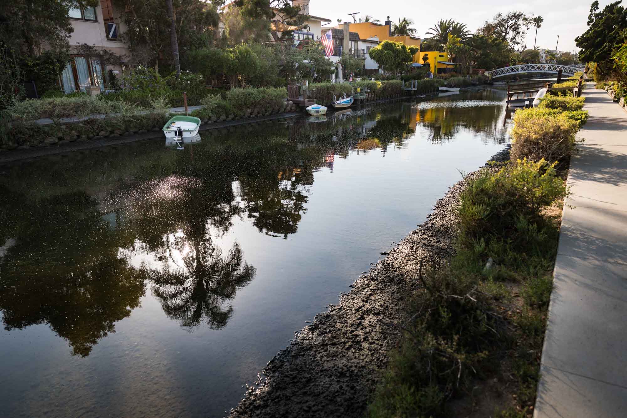 Venice Canal showing water at a low point and bottom of canal with sidewalk on the side and white footbridge in the background for an article on Venice Canals engagement photos