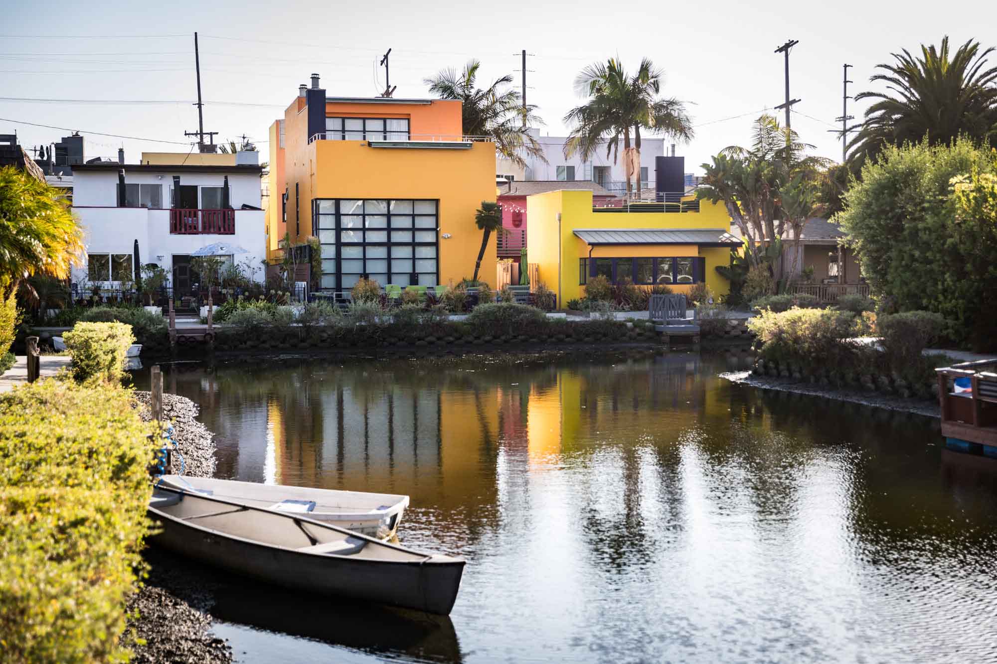 Venice Canal intersection with colorful houses in the background and two white rowboats parked on the side of the canal for an article on Venice Canals engagement photos