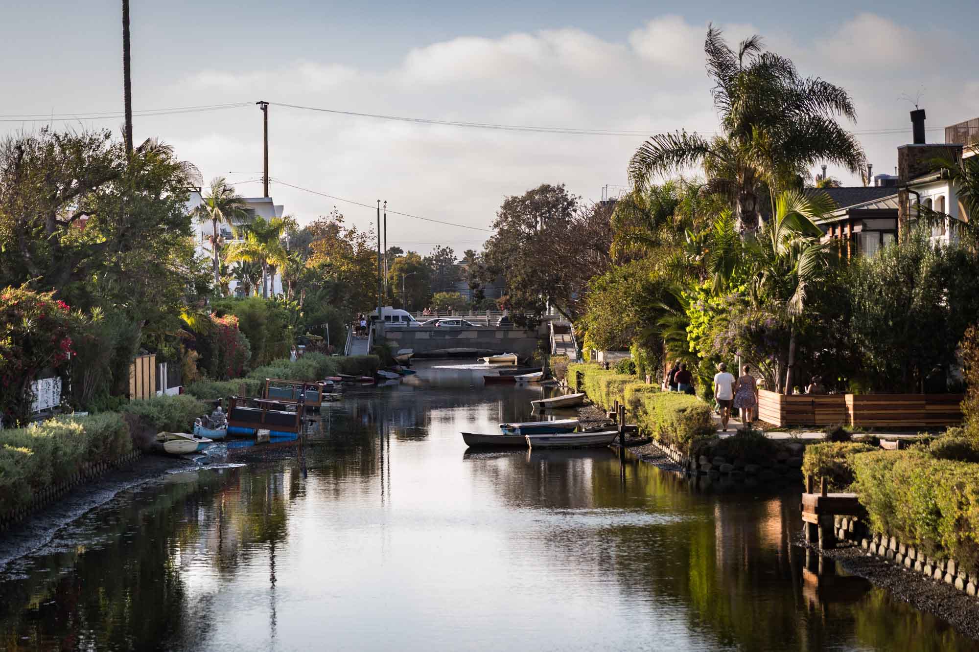 Bridge over a canal with boats, trees, and small docks on the side along the Venice Canals in Los Angeles for an article on Venice Canals engagement photos