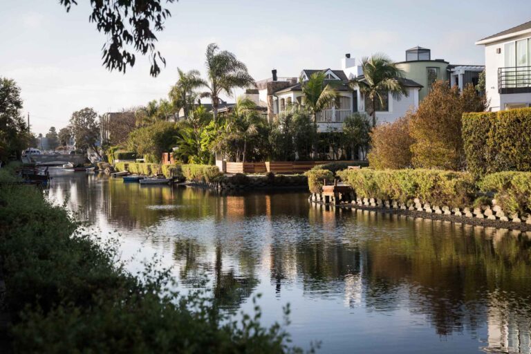 Bridge over a canal with boats, trees, and small docks on the side along the Venice Canals in Los Angeles for an article on Venice Canals engagement photos