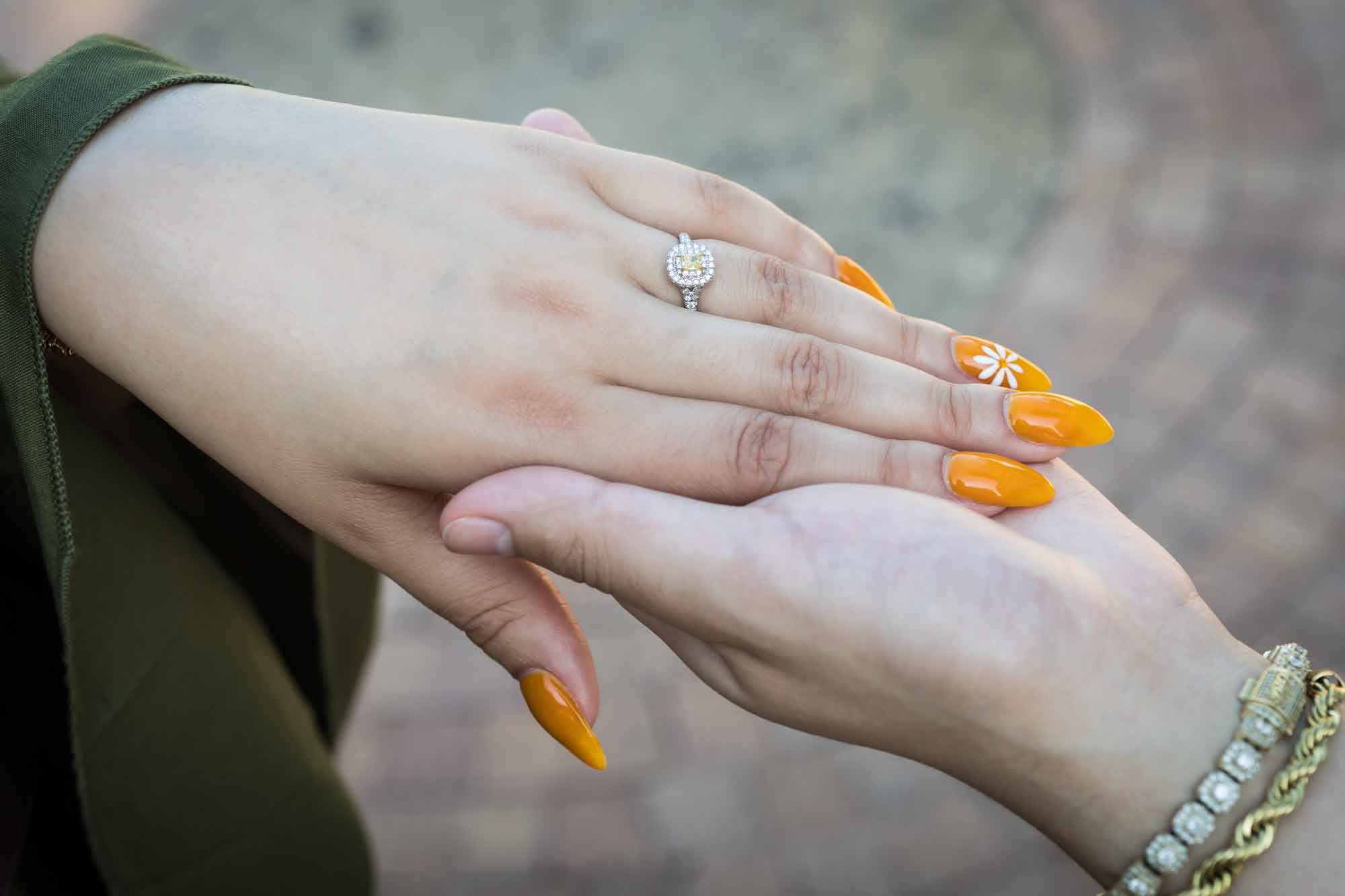 Close up of man holding woman's hand with yellow long nails and large yellow diamond engagement ring for an article on Venice Canals engagement photos