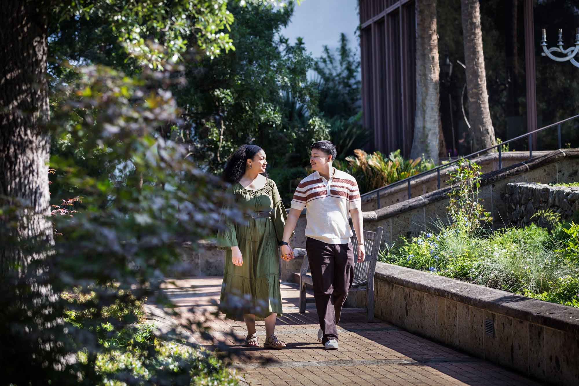Man and woman walking hand in hand along brick walkway in a garden for an article on Venice Canals engagement photos
