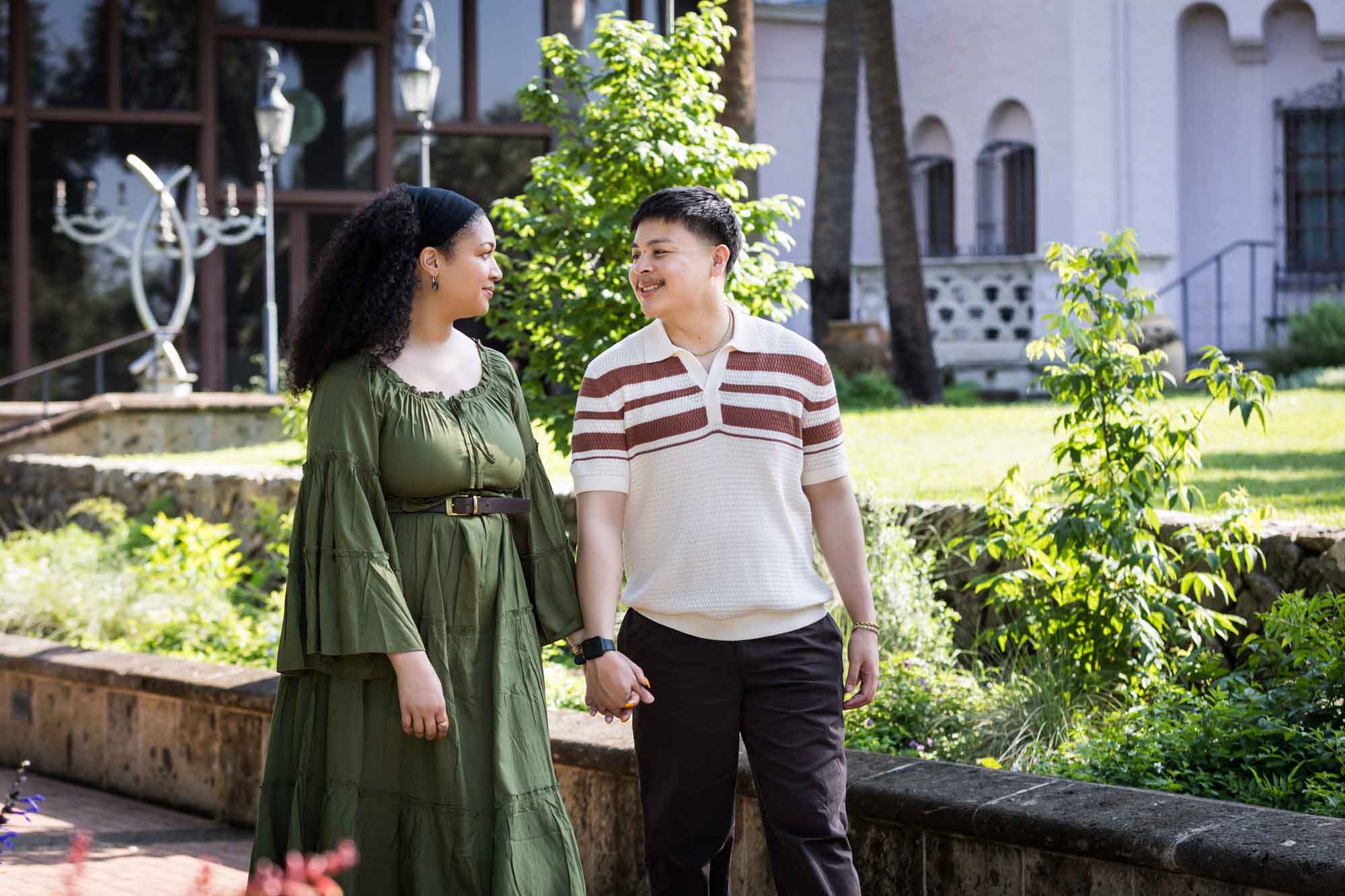 Man and woman walking hand in hand along brick walkway in a garden for an article on Venice Canals engagement photos