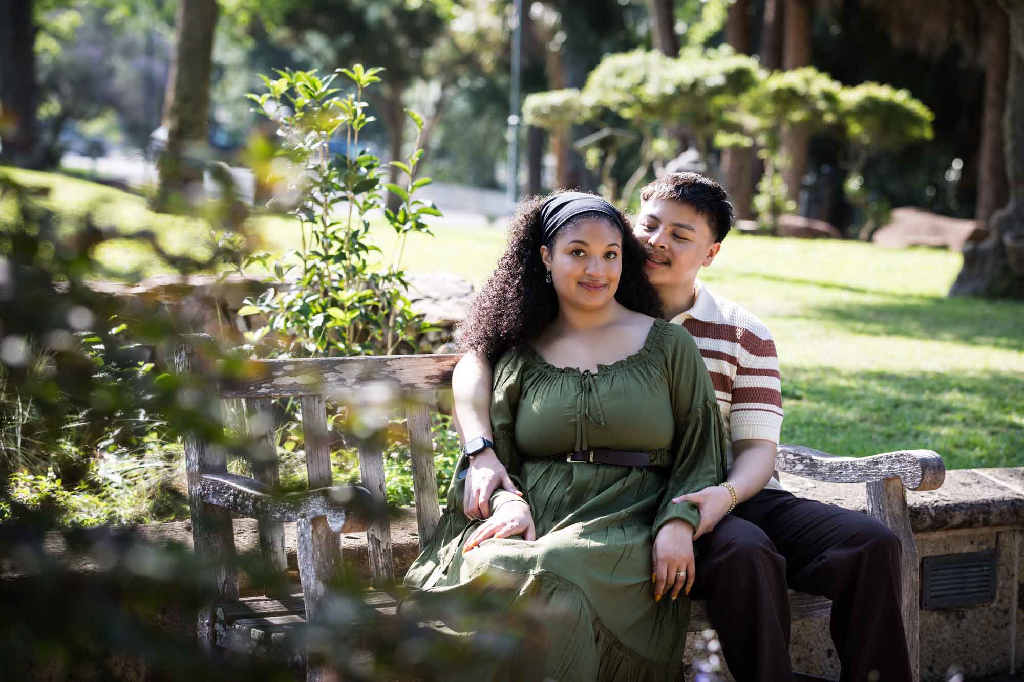 Man hugging woman while sitting together on wooden bench in a garden for an article on Venice Canals engagement photos