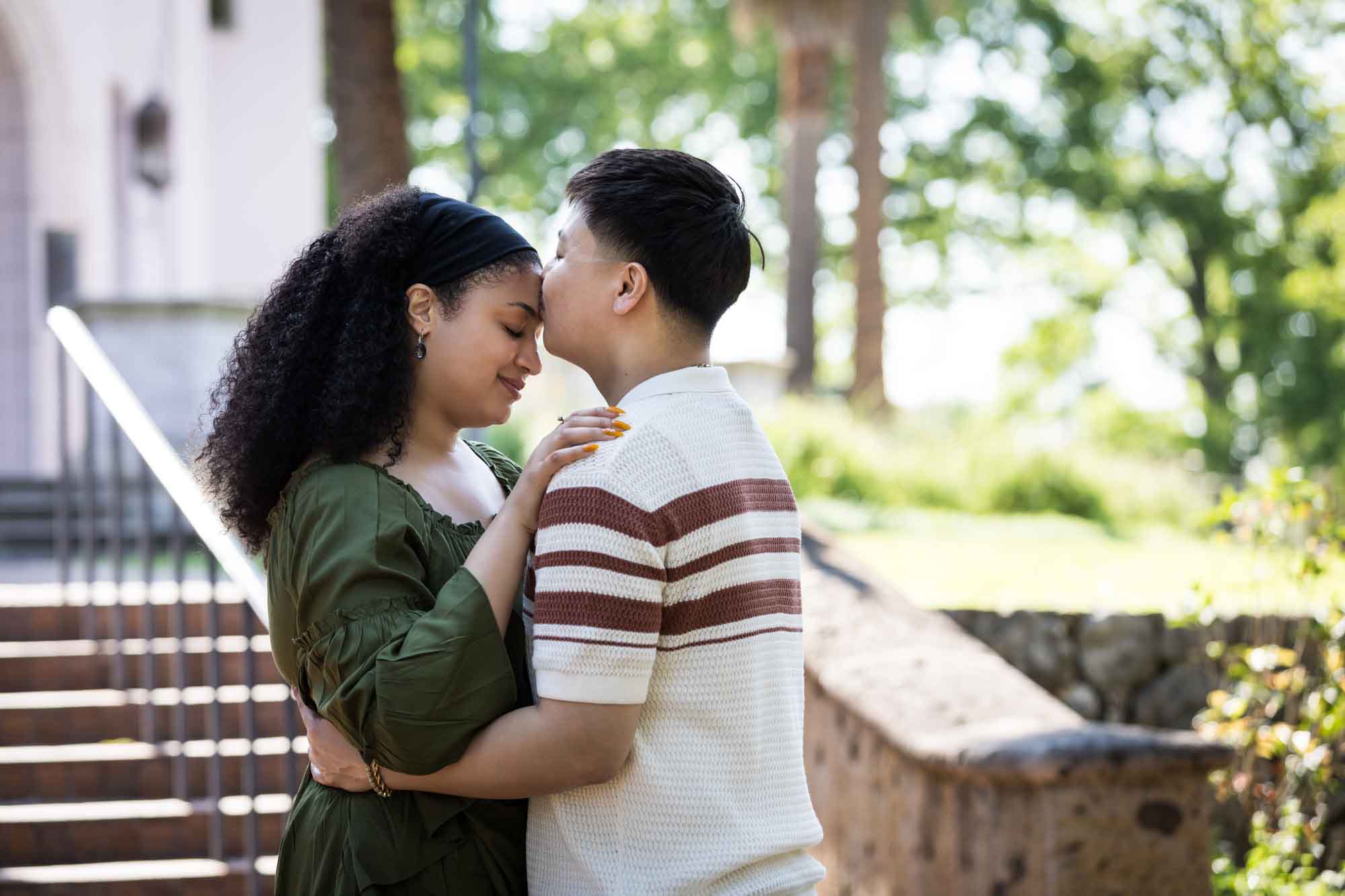 Man kissing woman on the forehead in front of stairs in a garden for an article on Venice Canals engagement photos