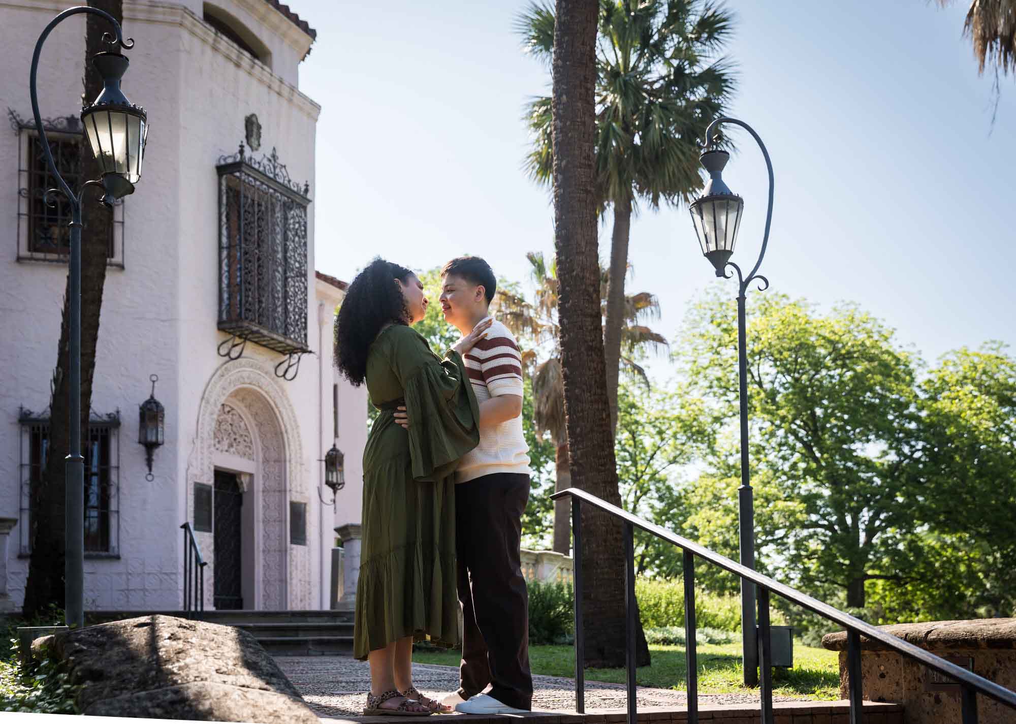 Man and woman hugging in front of intricate house and two antique lamp posts for an article on Venice Canals engagement photos
