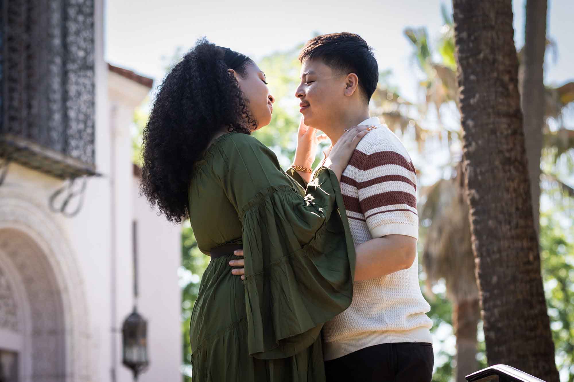 Man and woman hugging in front of intricate house and trees for an article on Venice Canals engagement photos