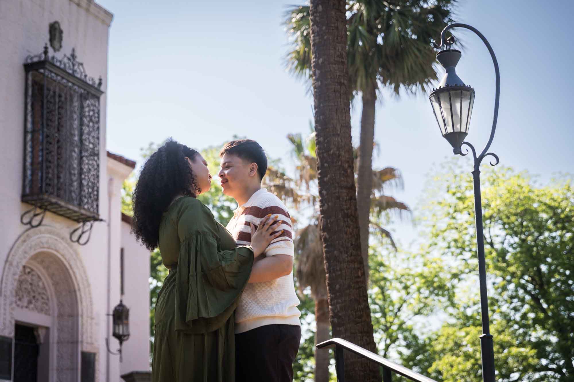 Man and woman hugging in front of intricate house and antique lamp post for an article on Venice Canals engagement photos