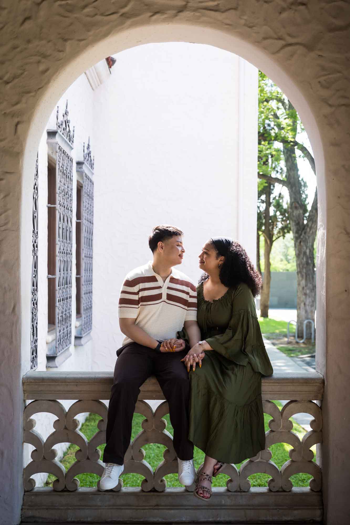 Man and woman sitting on latticework stone railing under stone arch window for an article on Venice Canals engagement photos