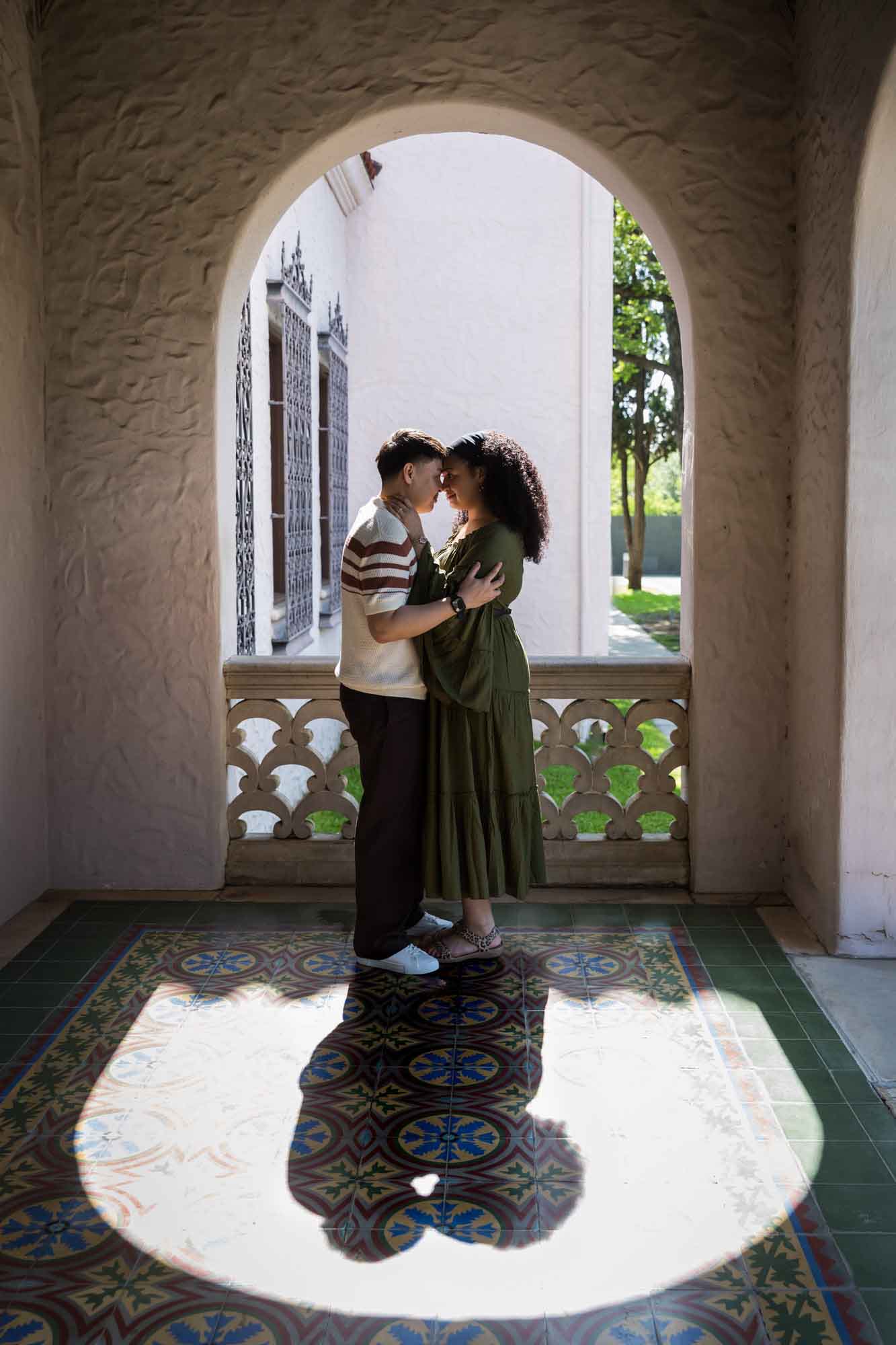 Man and woman standing with foreheads together in middle of stone arch window with shadow for an article on Venice Canals engagement photos