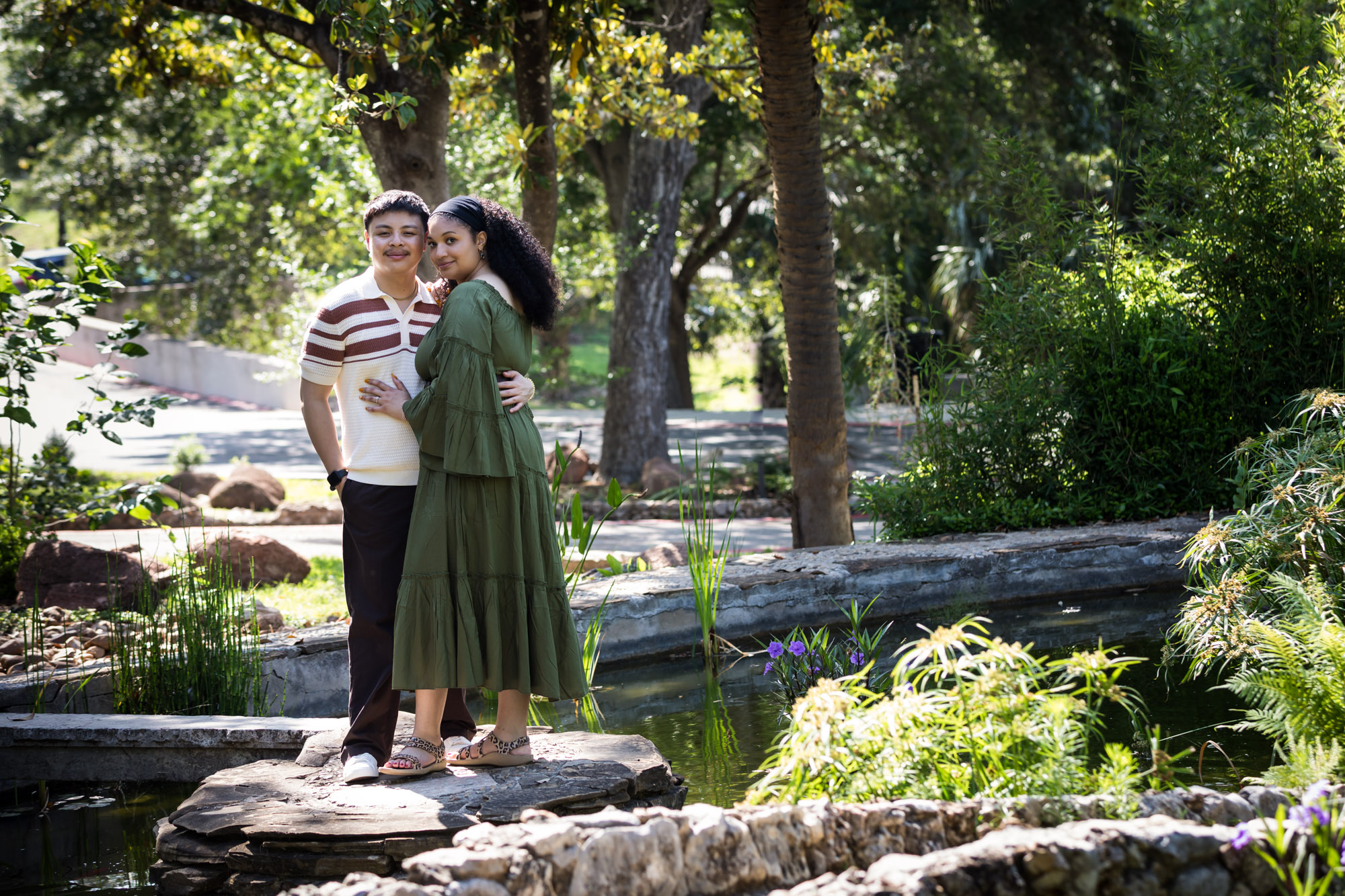 Woman wearing green dress standing with man on stone island in garden lake for an article on Venice Canals engagement photos