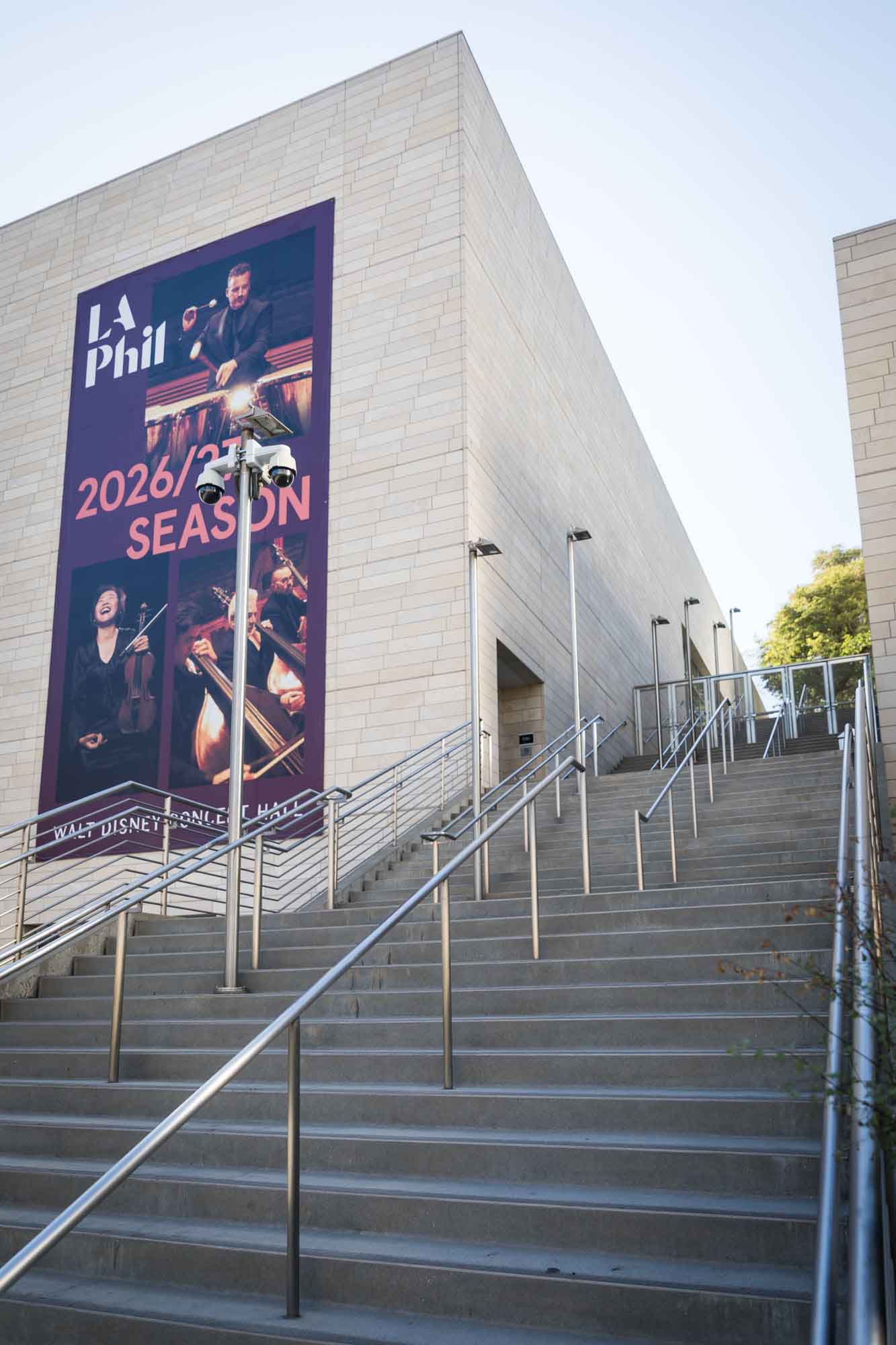 Side grand staircase with brick stone wall and sign announcing LA Philharmonic 2026/27 season for an article on Walt Disney Concert Hall photos