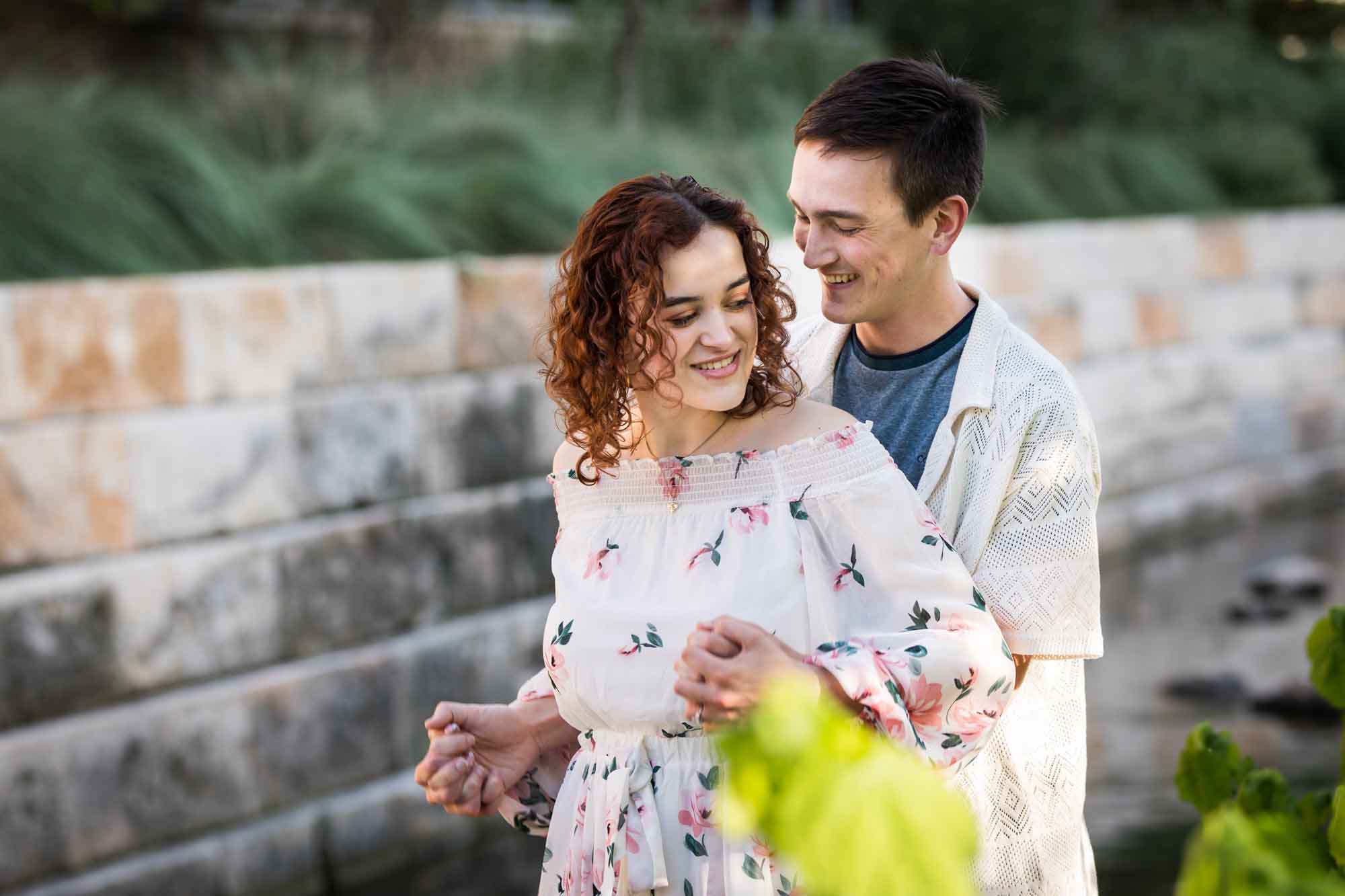 Man holding hands with woman from behind with large brick wall and green plants in background for an article on Walt Disney Concert Hall photos