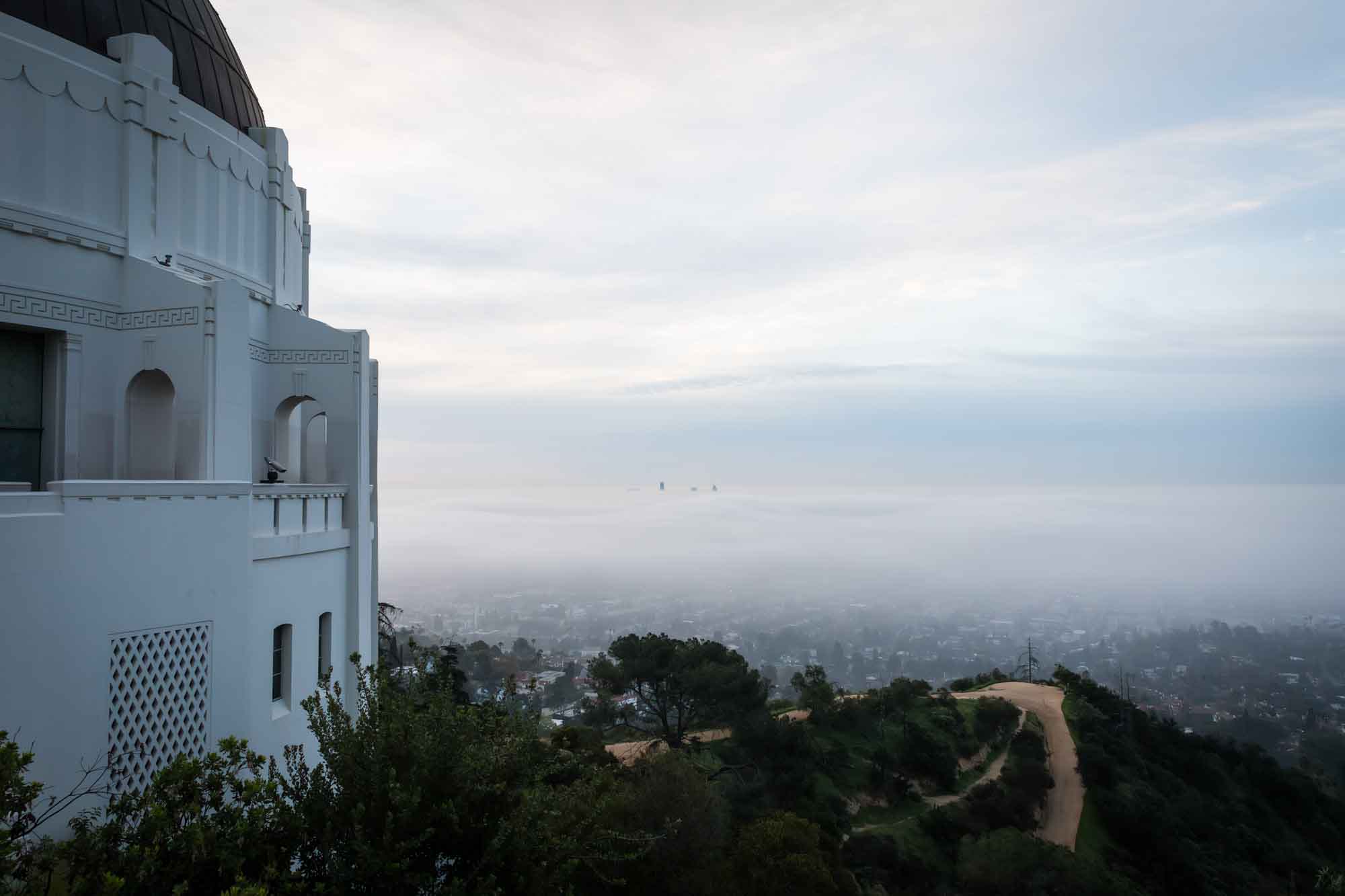 Side profile of Griffith Observatory and view of Los Angeles skyline through fog before sunrise for an article on where to propose at the Griffith Observatory