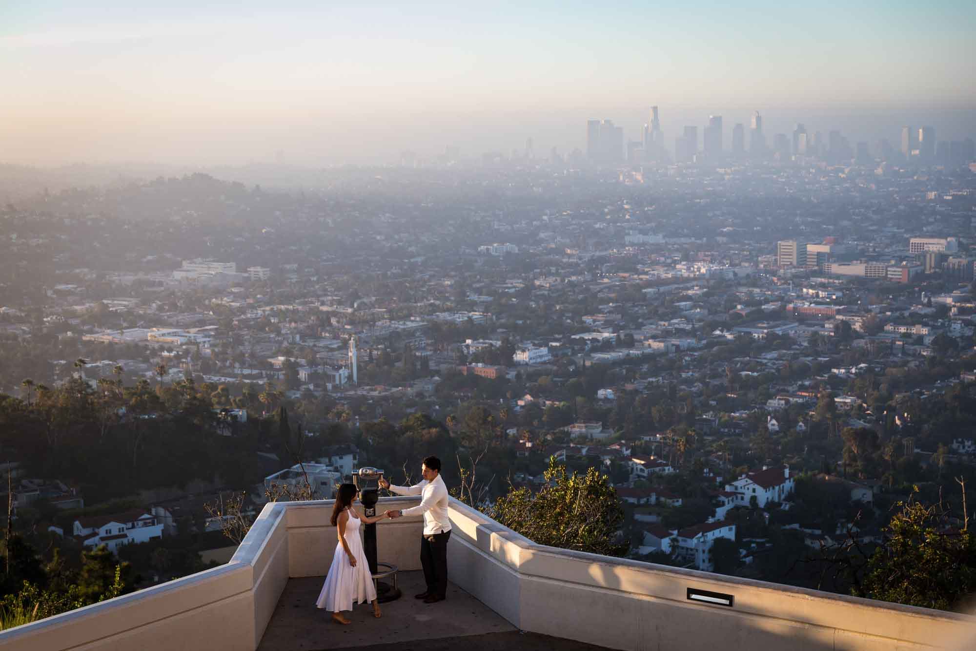 Engaged couple standing in front of binoculars on East Terrace at sunrise for an article on where to propose at the Griffith Observatory