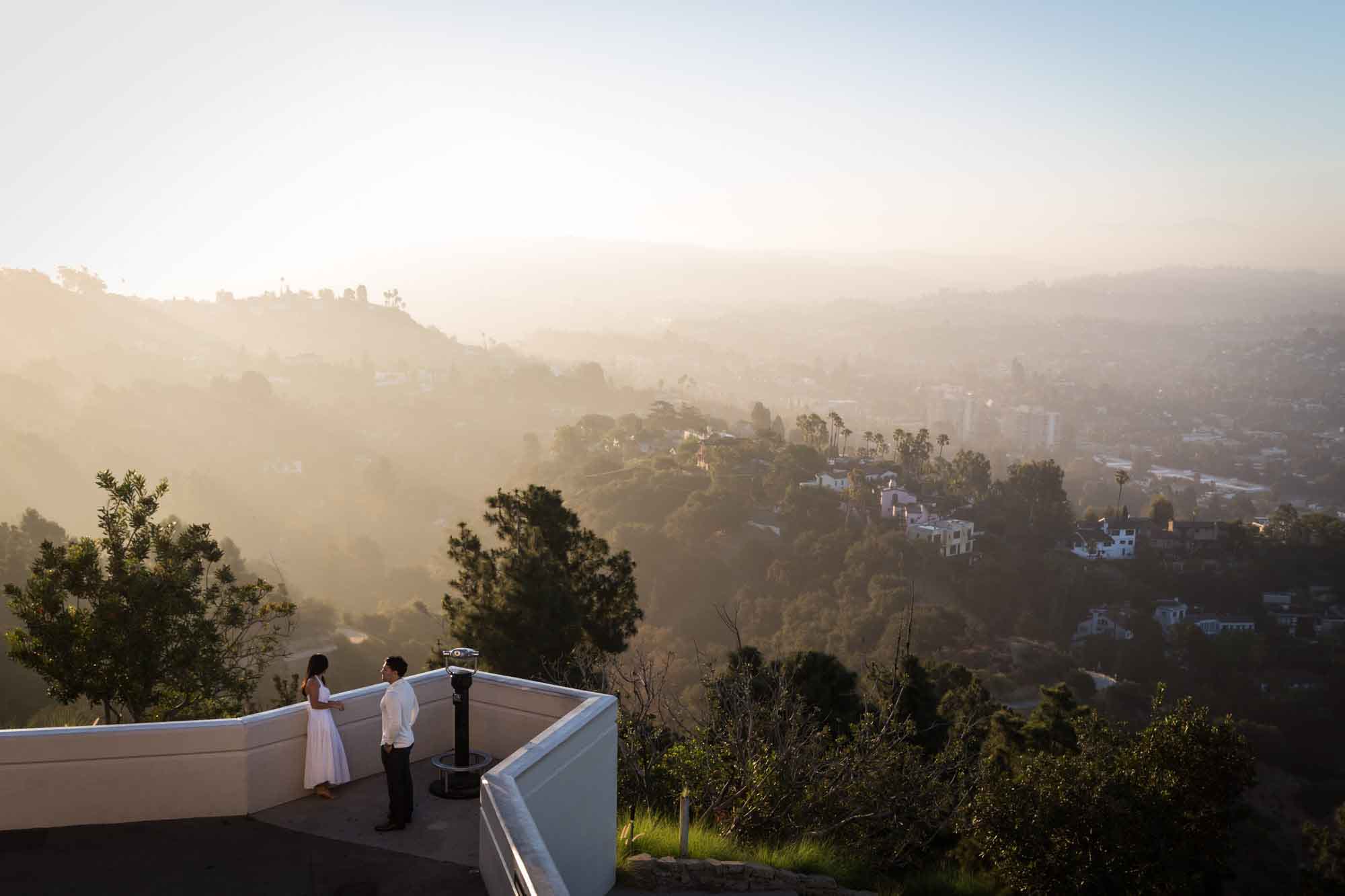 Engaged couple standing in front of binoculars on East Terrace at sunrise for an article on where to propose at the Griffith Observatory