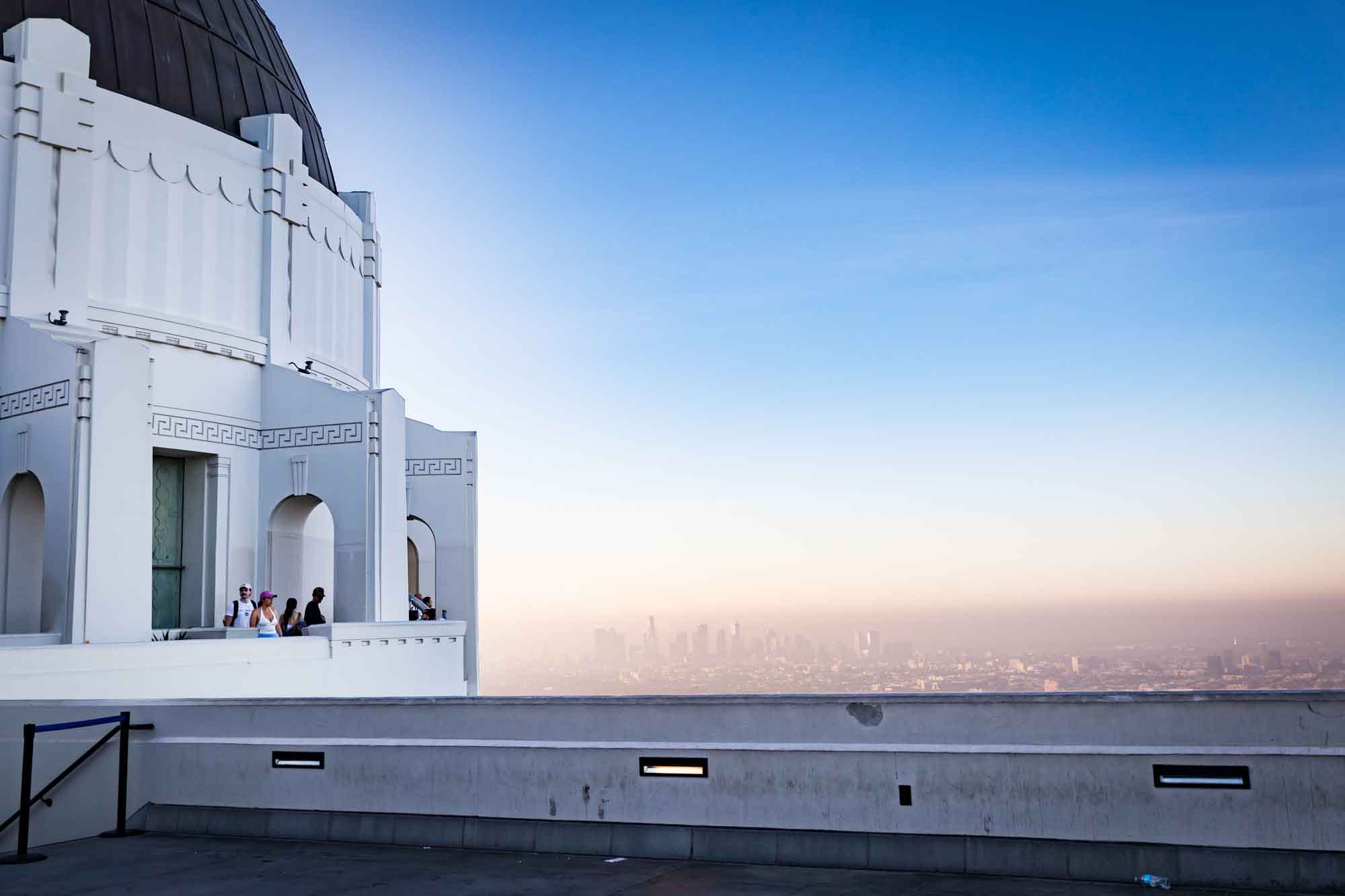 West Terrace and guests standing on side of roof of Griffith Observatory with Los Angeles downtown skyline in the background for an article on where to propose at the Griffith Observatory