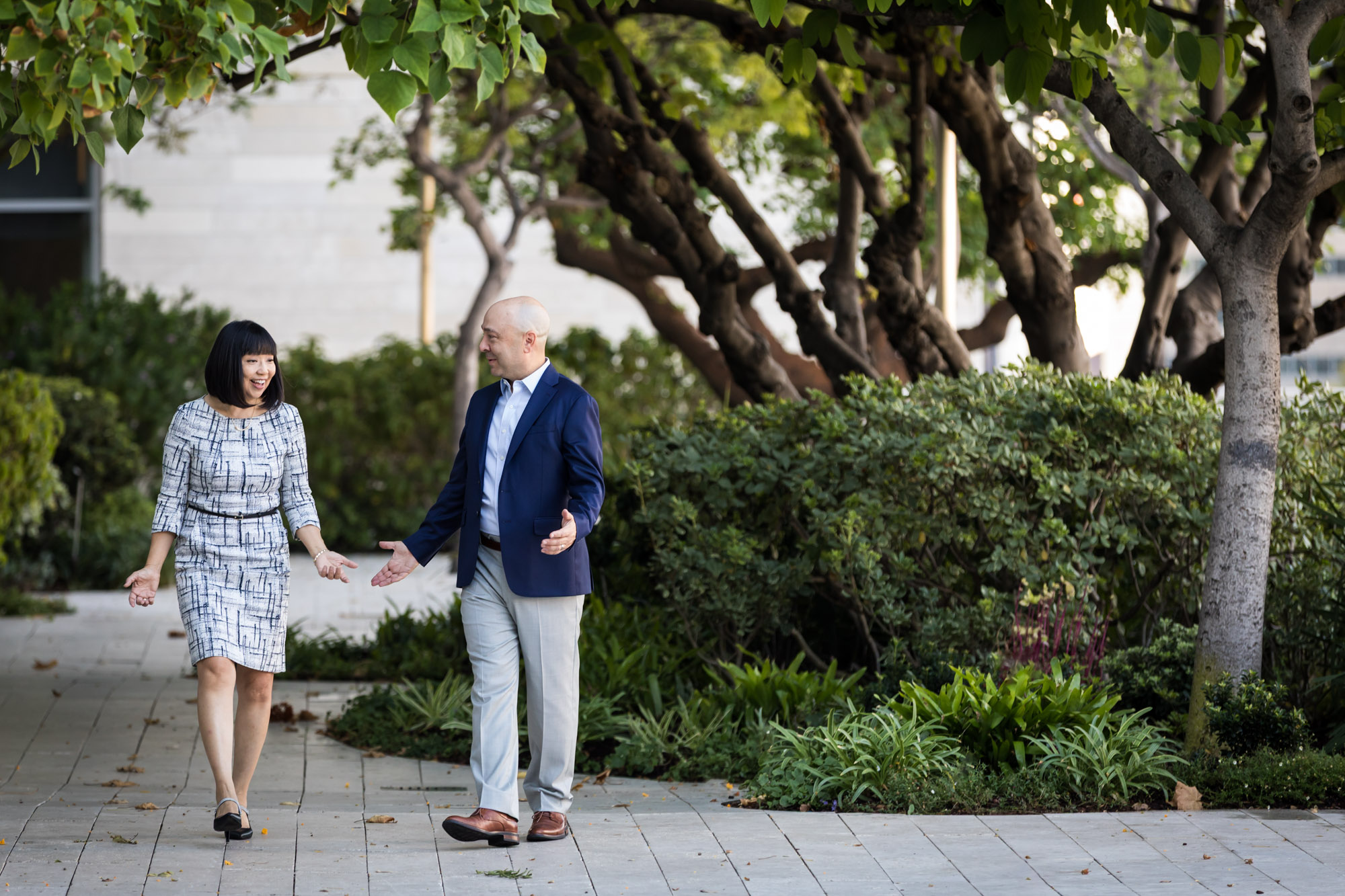 Businessman wearing blue jacket and khaki pants walking and talking with Asian American female colleague wearing dress in Blue Ribbon Garden for an article on how to prepare for a branding photo shoot