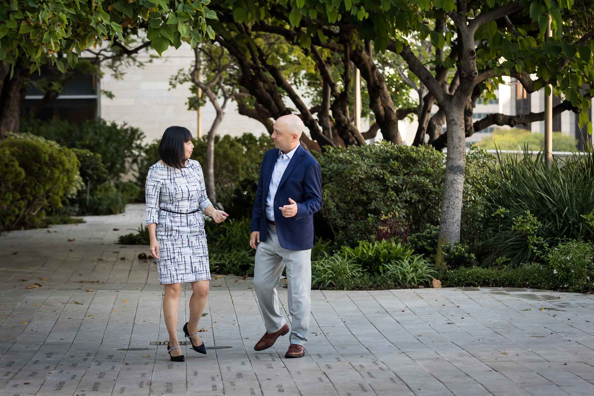 Businessman wearing blue jacket and khaki pants walking and talking with Asian American female colleague wearing dress in Blue Ribbon Garden for an article on how to prepare for a branding photo shoot