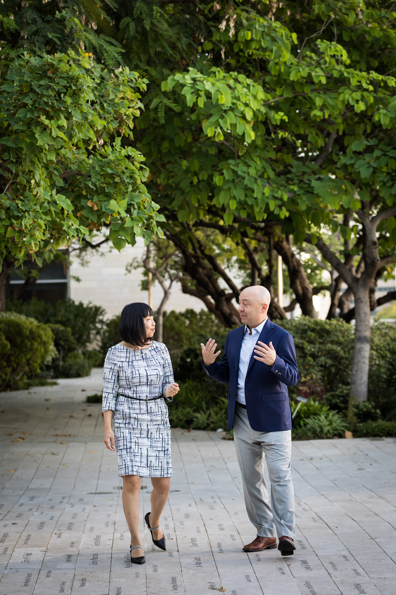 Businessman wearing blue jacket and khaki pants walking and talking with Asian American female colleague wearing dress in Blue Ribbon Garden for an article on how to prepare for a branding photo shoot