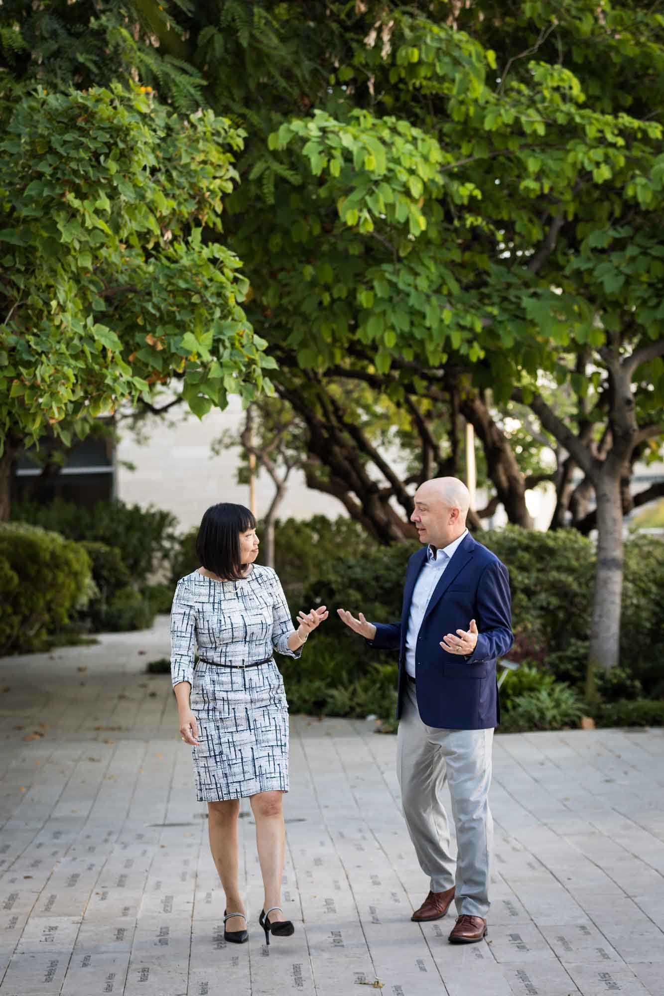 Businessman wearing blue jacket and khaki pants walking and talking with Asian American female colleague wearing dress in Blue Ribbon Garden for an article on how to prepare for a branding photo shoot