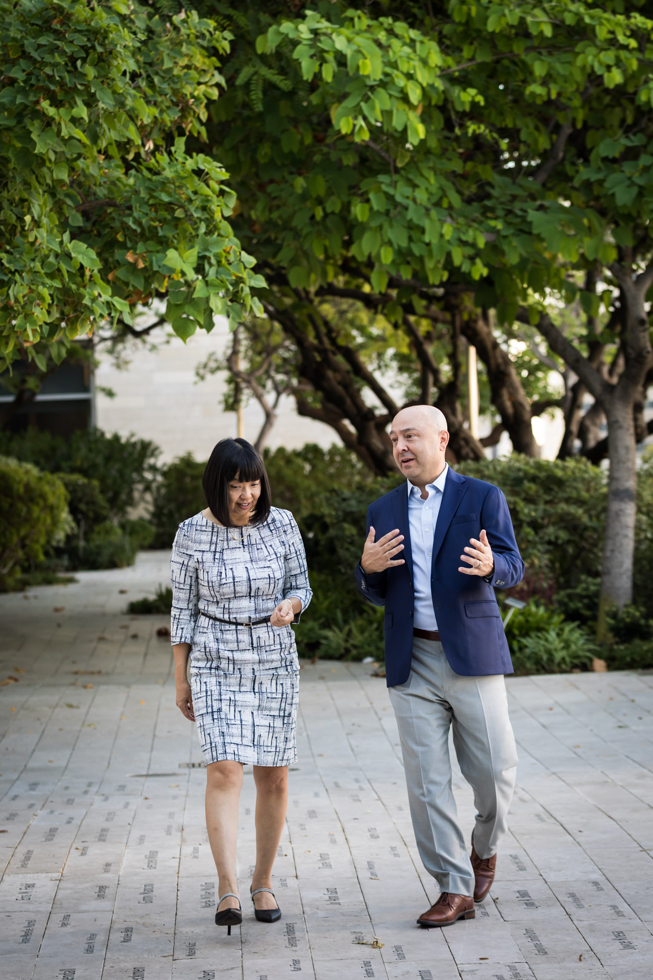 Businessman wearing blue jacket and khaki pants walking and talking with Asian American female colleague wearing dress in Blue Ribbon Garden for an article on how to prepare for a branding photo shoot