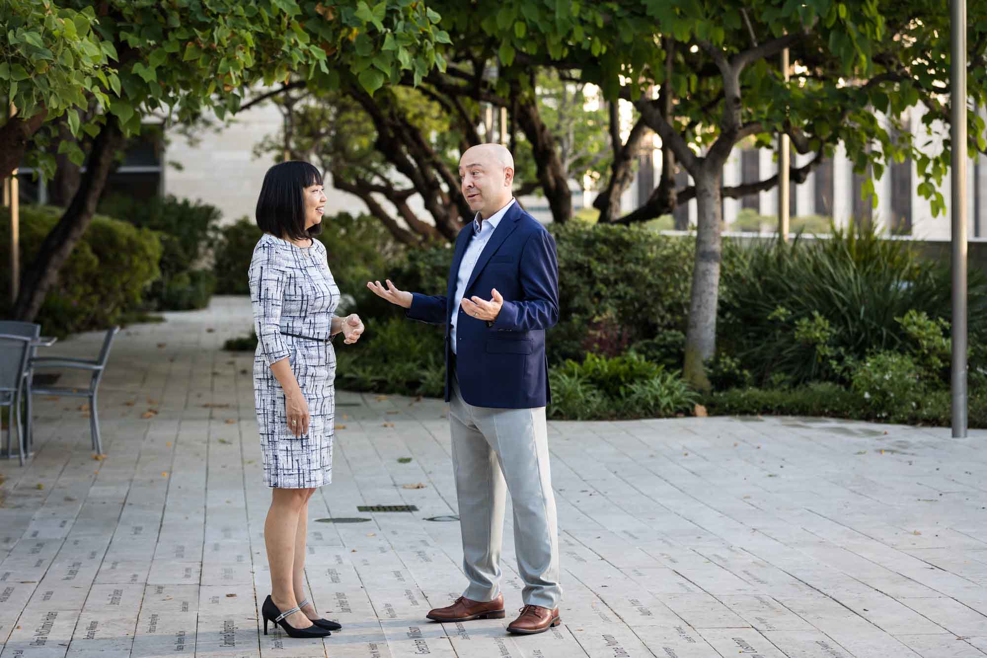Businessman wearing blue jacket and khaki pants walking and talking with Asian American female colleague wearing dress in Blue Ribbon Garden for an article on how to prepare for a branding photo shoot
