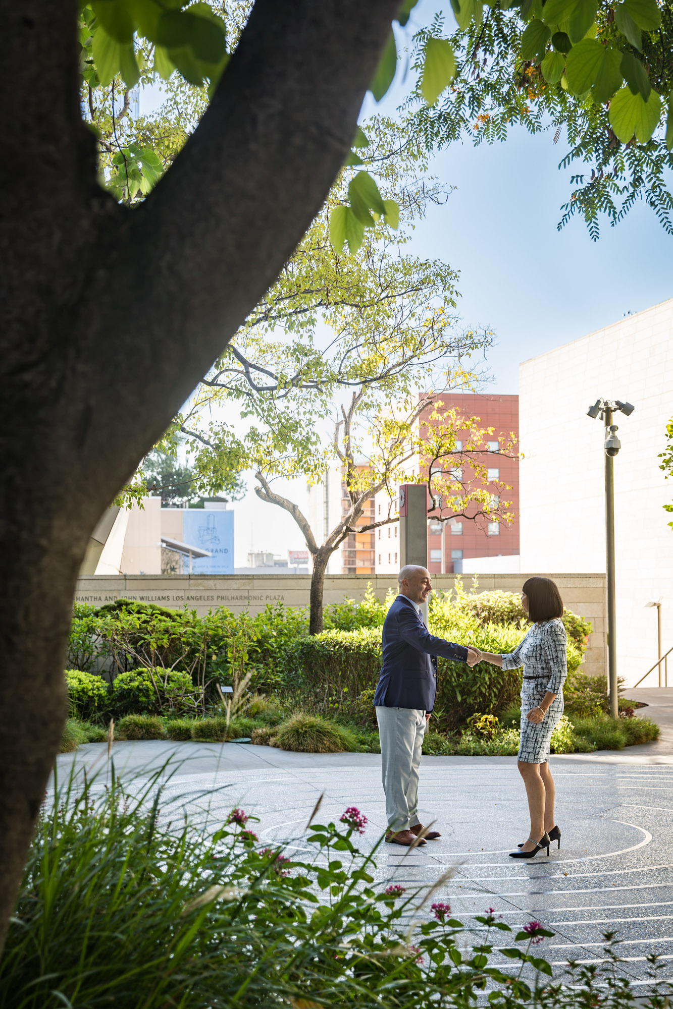 Businessman wearing blue jacket and khaki pants walking and talking with Asian American female colleague wearing dress in Blue Ribbon Garden for an article on how to prepare for a branding photo shoot