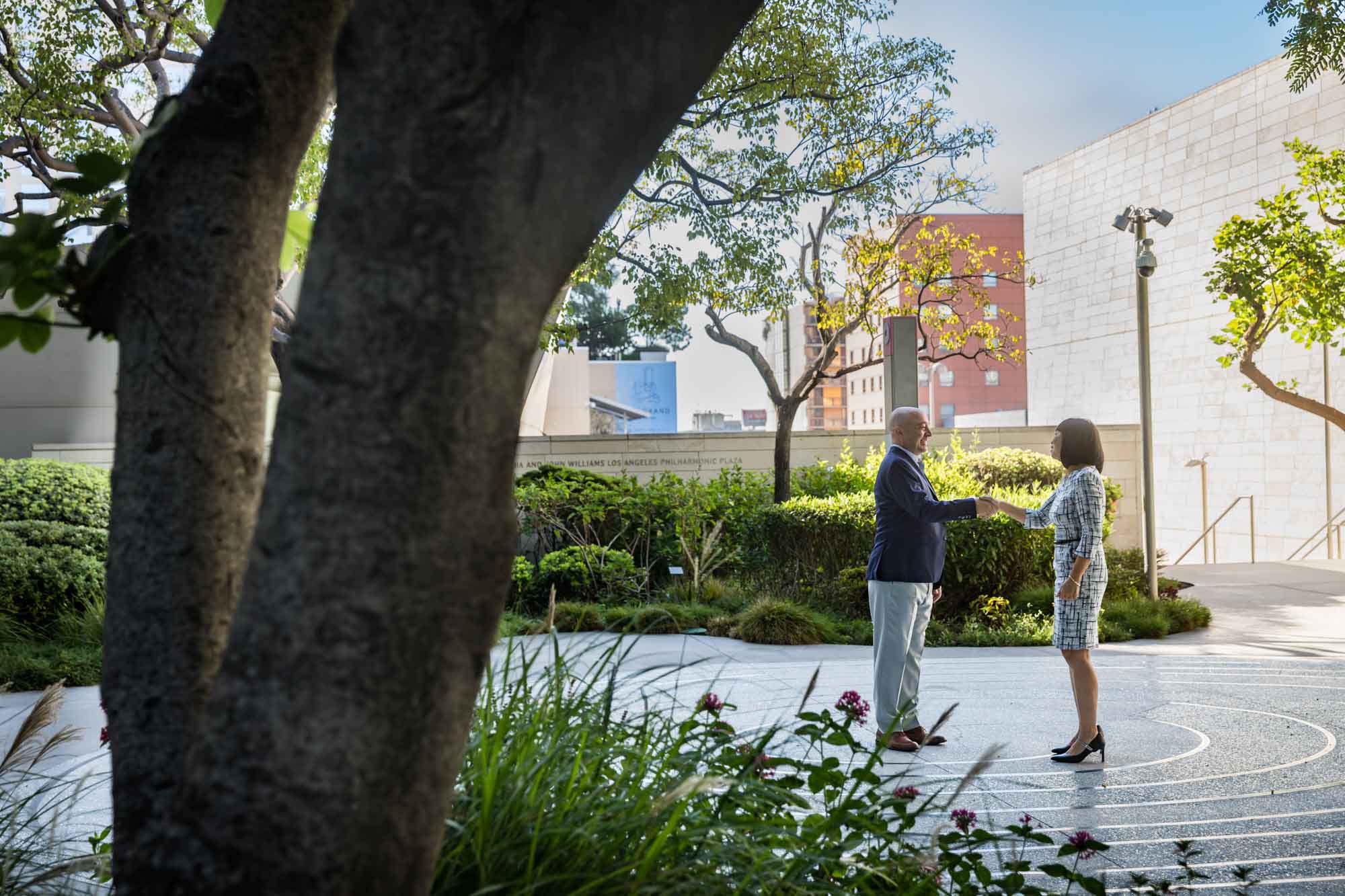 Businessman wearing blue jacket and khaki pants walking and talking with Asian American female colleague wearing dress in Blue Ribbon Garden for an article on how to prepare for a branding photo shoot