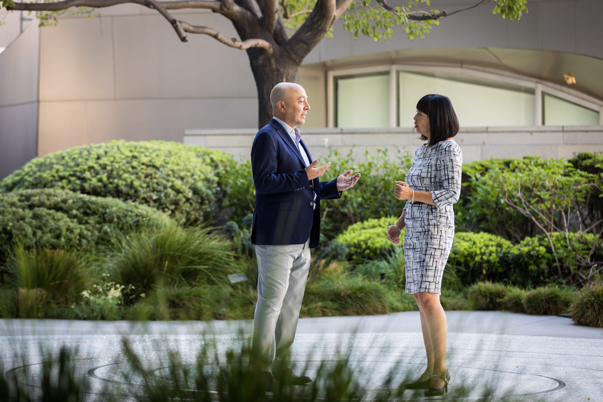 Businessman wearing blue jacket and khaki pants walking and talking with Asian American female colleague wearing dress in Blue Ribbon Garden for an article on how to prepare for a branding photo shoot