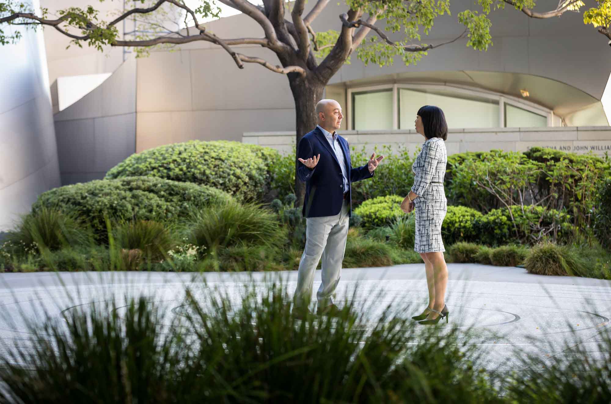 Businessman wearing blue jacket and khaki pants walking and talking with Asian American female colleague wearing dress in Blue Ribbon Garden for an article on how to prepare for a branding photo shoot