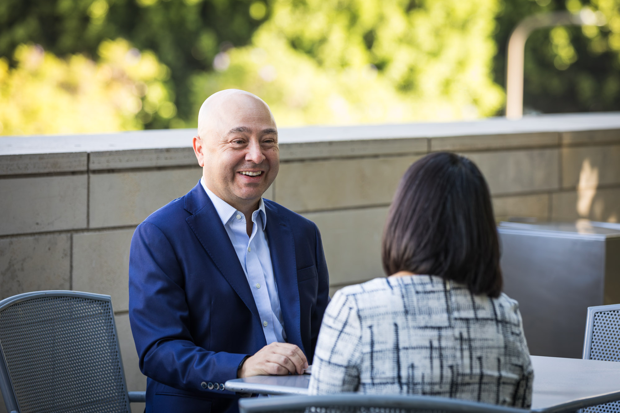 Businessman wearing blue jacket and khaki pants seated and talking with Asian American female colleague wearing dress in Blue Ribbon Garden for an article on how to prepare for a branding photo shoot