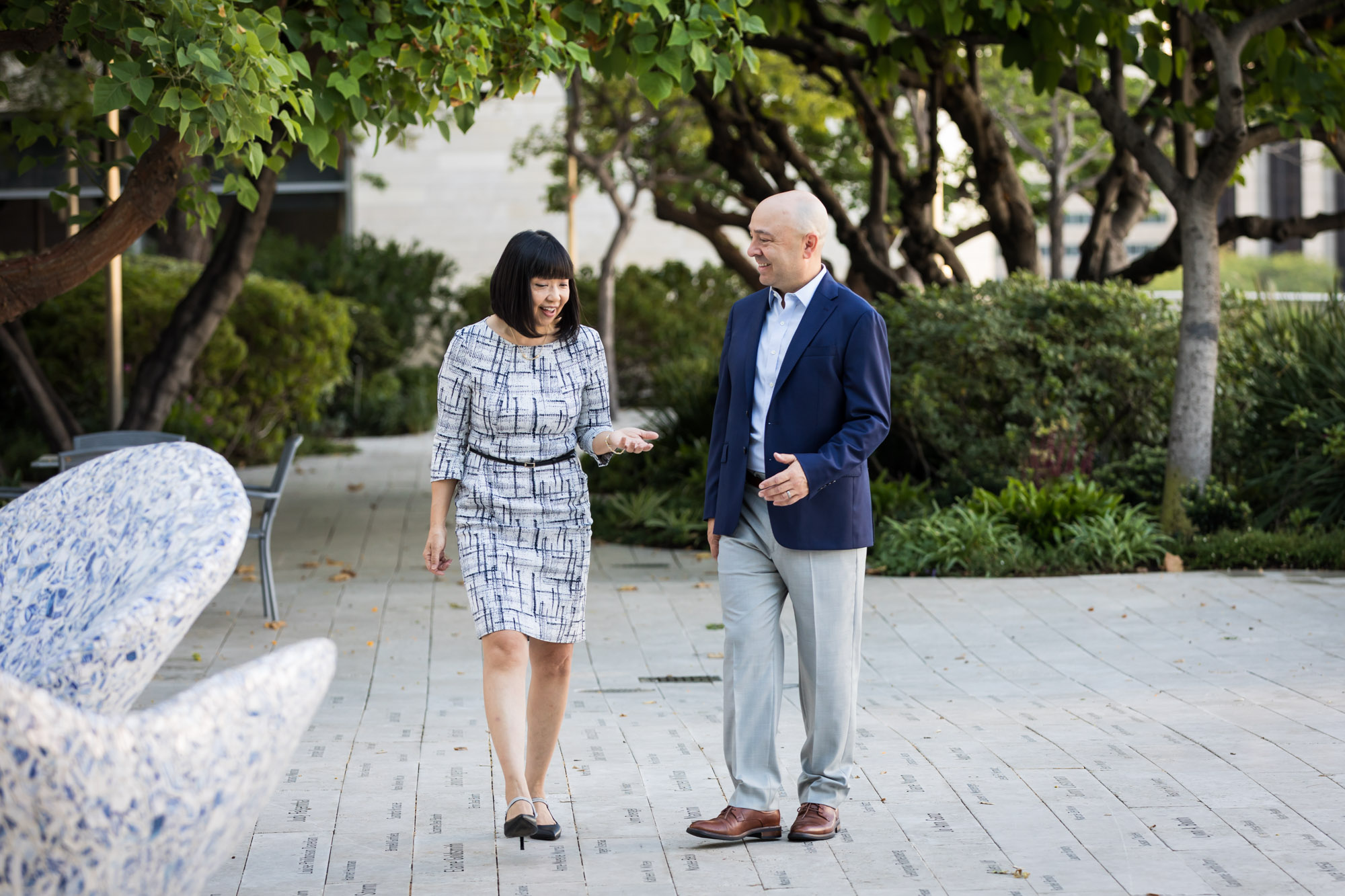 Businessman wearing blue jacket and khaki pants walking and talking with Asian American female colleague wearing dress in Blue Ribbon Garden for an article on how to prepare for a branding photo shoot