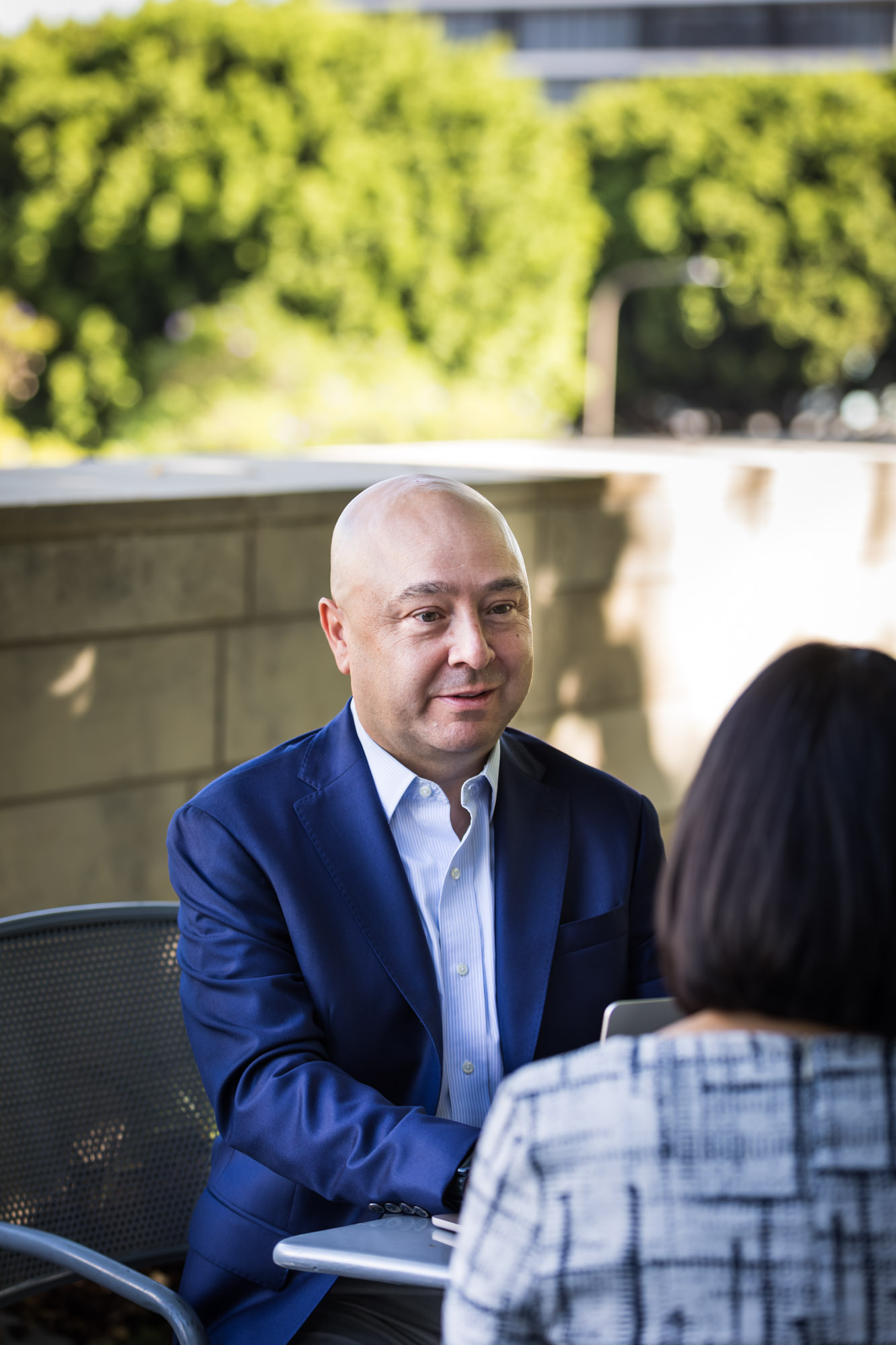 Businessman wearing blue jacket and khaki pants seated and talking with Asian American female colleague wearing dress in Blue Ribbon Garden for an article on how to prepare for a branding photo shoot