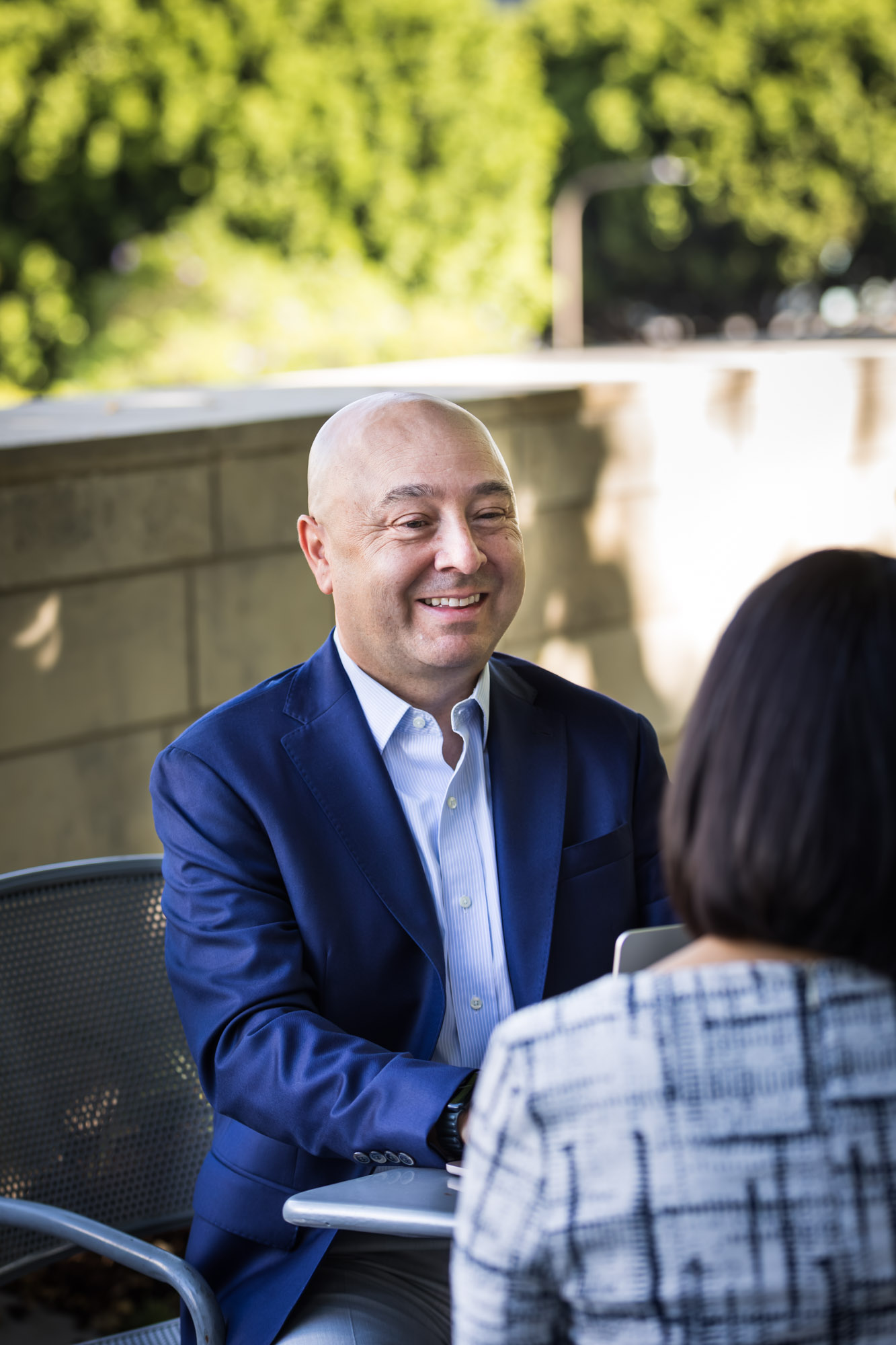 Businessman wearing blue jacket and khaki pants seated and talking with Asian American female colleague wearing dress in Blue Ribbon Garden for an article on how to prepare for a branding photo shoot