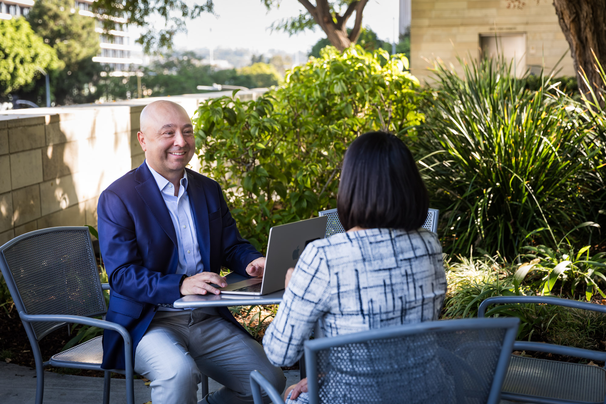 Businessman wearing blue jacket and khaki pants seated and talking with Asian American female colleague wearing dress in Blue Ribbon Garden for an article on how to prepare for a branding photo shoot