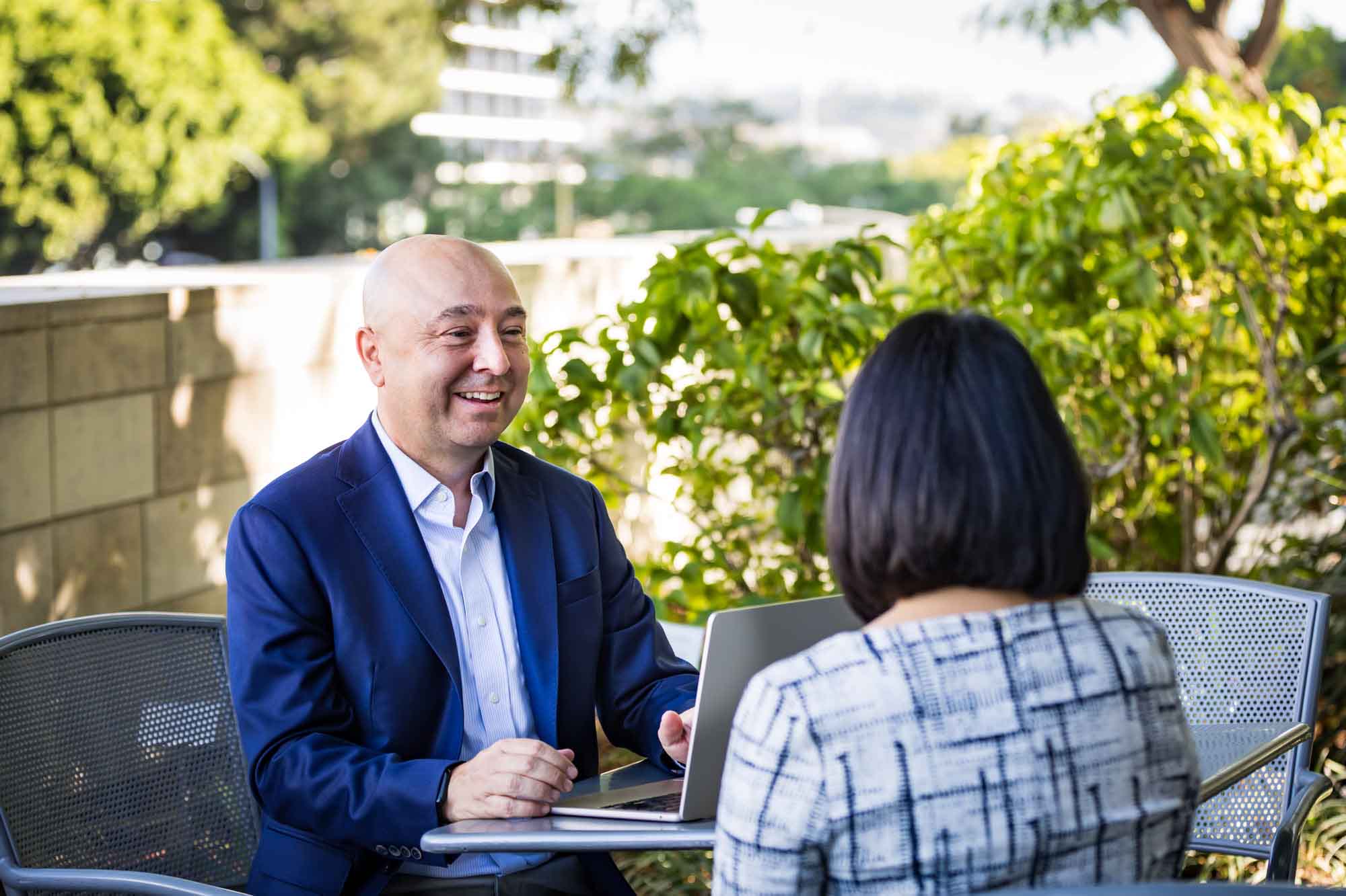 Businessman wearing blue jacket and khaki pants seated and talking with Asian American female colleague wearing dress in Blue Ribbon Garden for an article on how to prepare for a branding photo shoot
