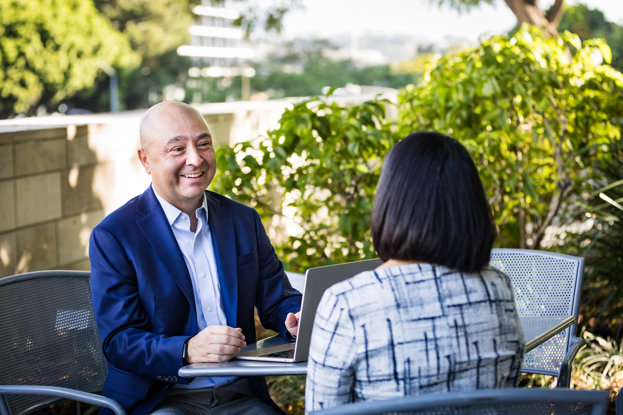 Businessman wearing blue jacket and khaki pants seated and talking with Asian American female colleague wearing dress in Blue Ribbon Garden for an article on how to prepare for a branding photo shoot