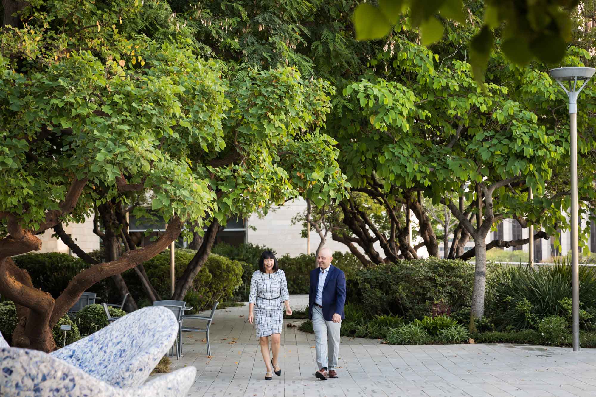 Businessman wearing blue jacket and khaki pants walking and talking with Asian American female colleague wearing dress in Blue Ribbon Garden for an article on how to prepare for a branding photo shoot