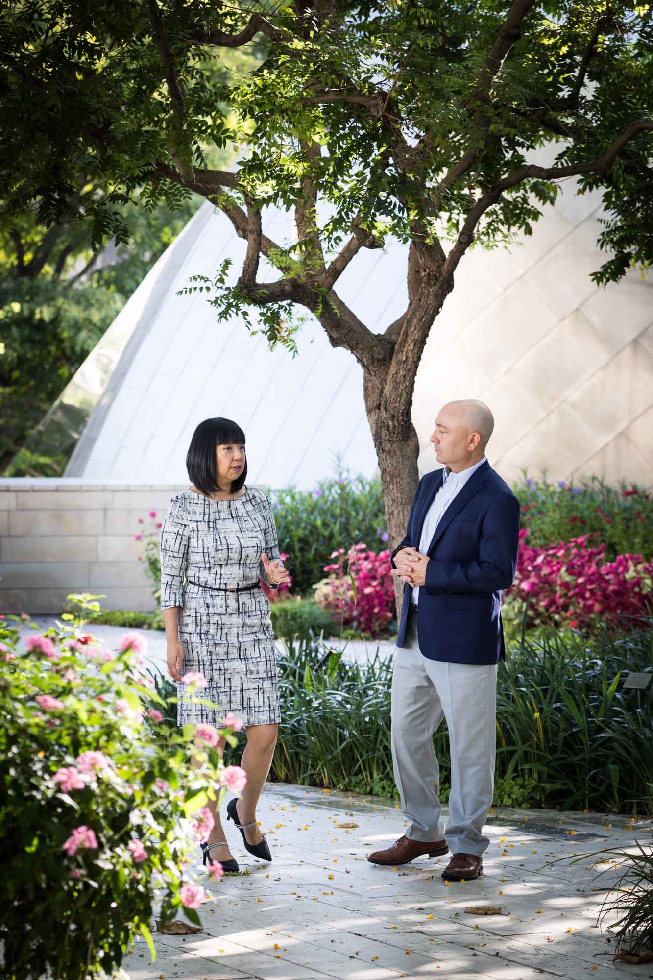 Businessman wearing blue jacket and khaki pants walking and talking with Asian American female colleague wearing dress in Blue Ribbon Garden for an article on how to prepare for a branding photo shoot
