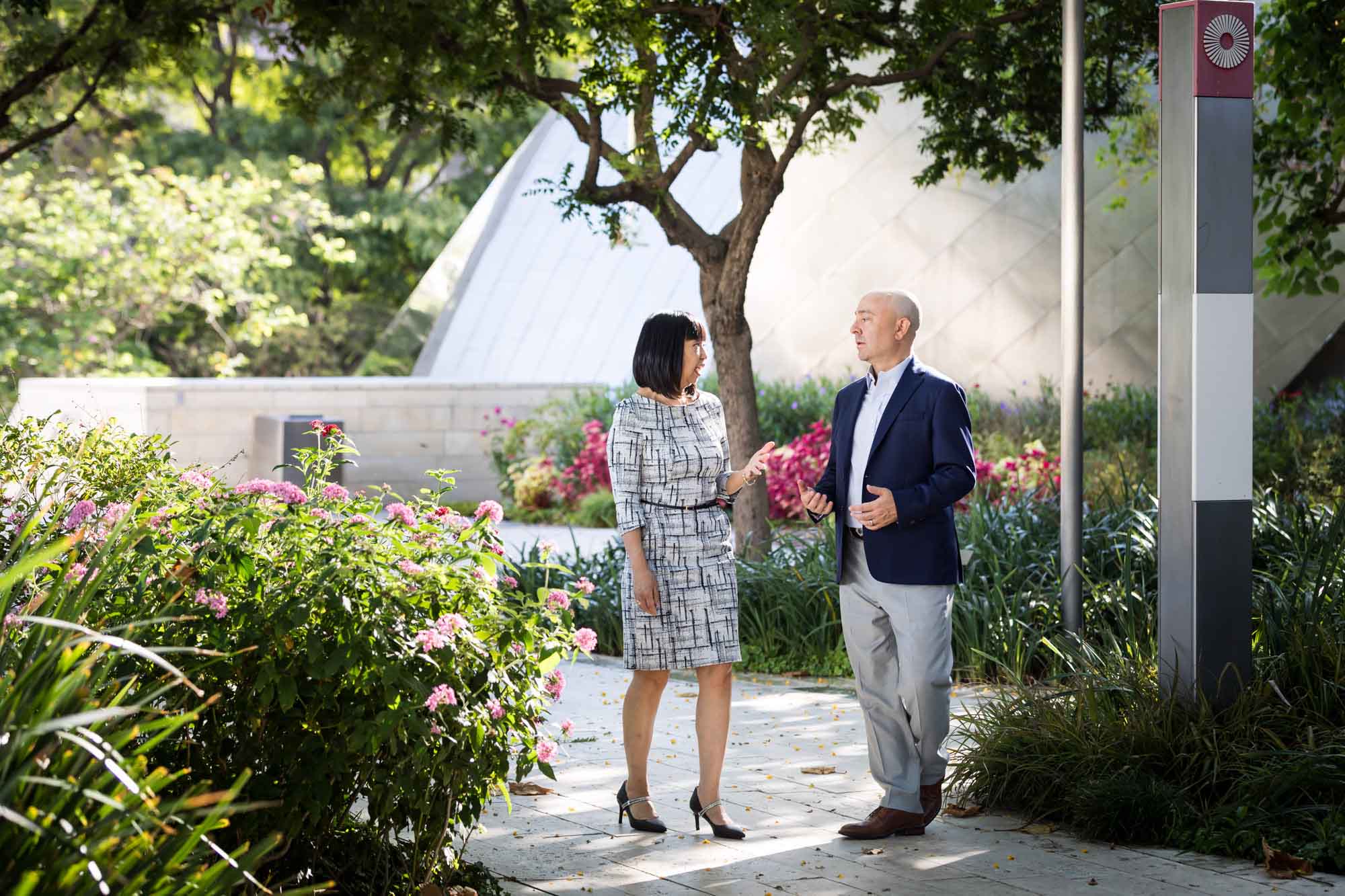 Businessman wearing blue jacket and khaki pants walking and talking with Asian American female colleague wearing dress in Blue Ribbon Garden for an article on how to prepare for a branding photo shoot