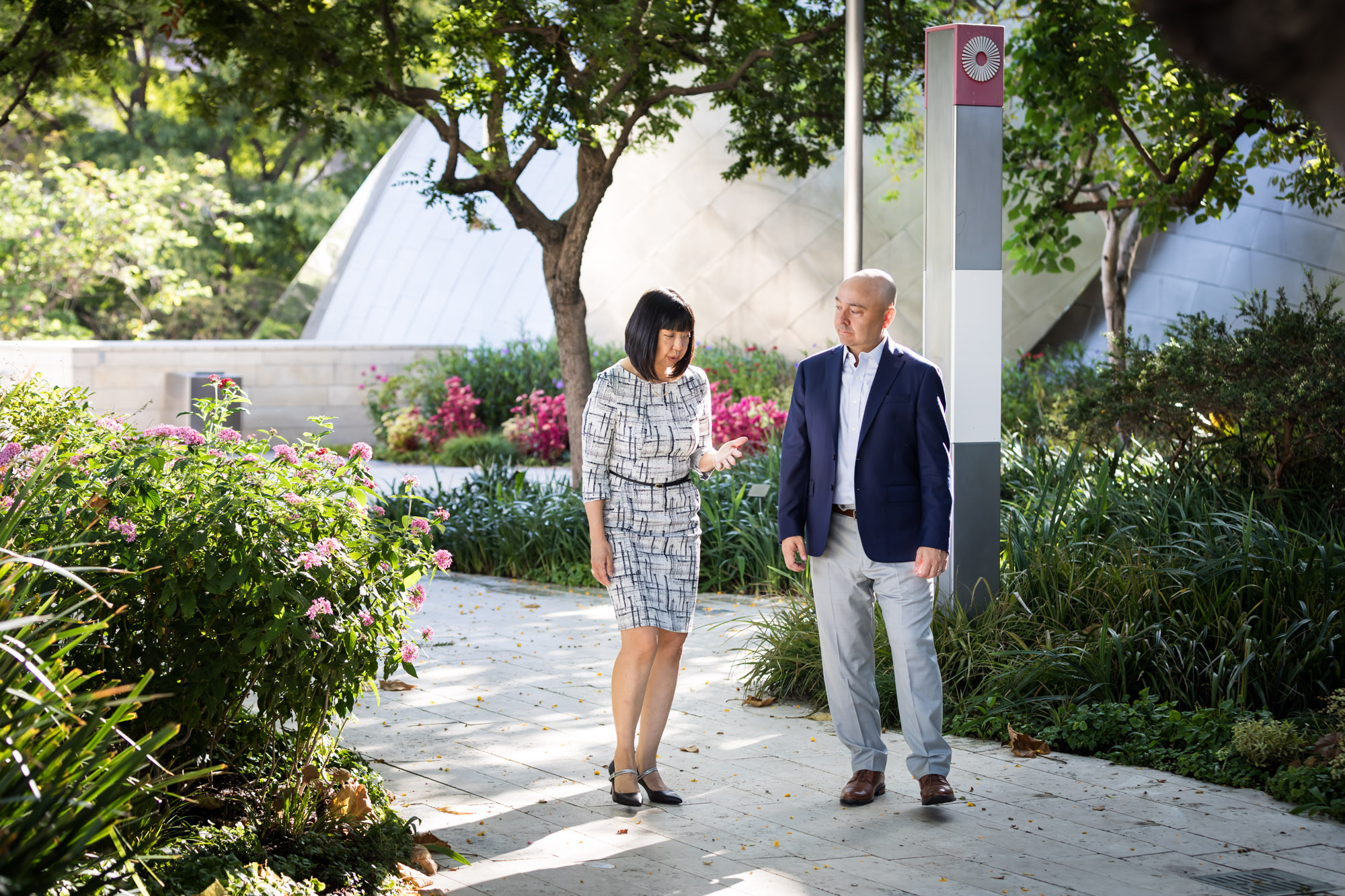 Businessman wearing blue jacket and khaki pants walking and talking with Asian American female colleague wearing dress in Blue Ribbon Garden for an article on how to prepare for a branding photo shoot