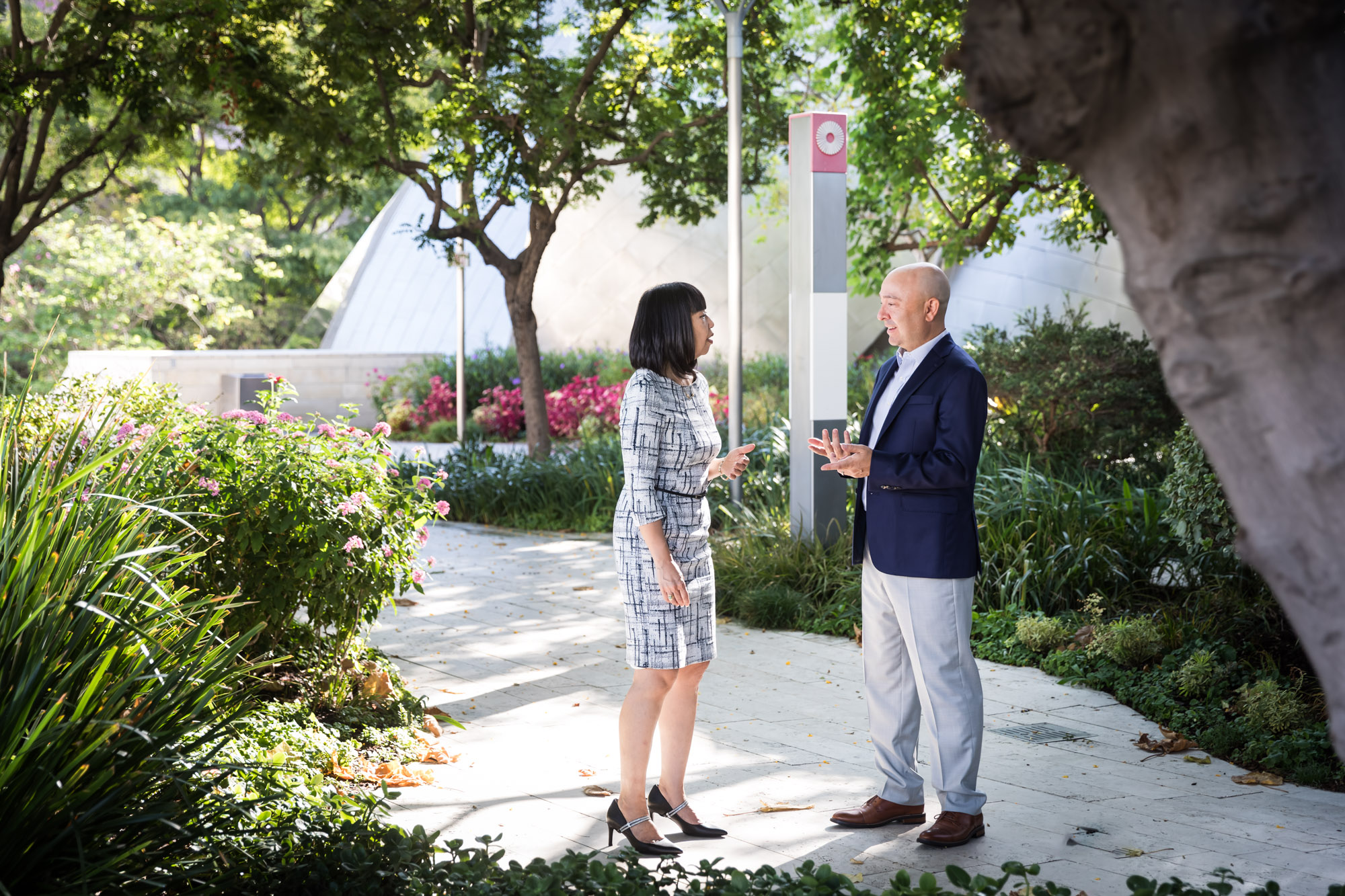 Businessman wearing blue jacket and khaki pants walking and talking with Asian American female colleague wearing dress in Blue Ribbon Garden for an article on how to prepare for a branding photo shoot