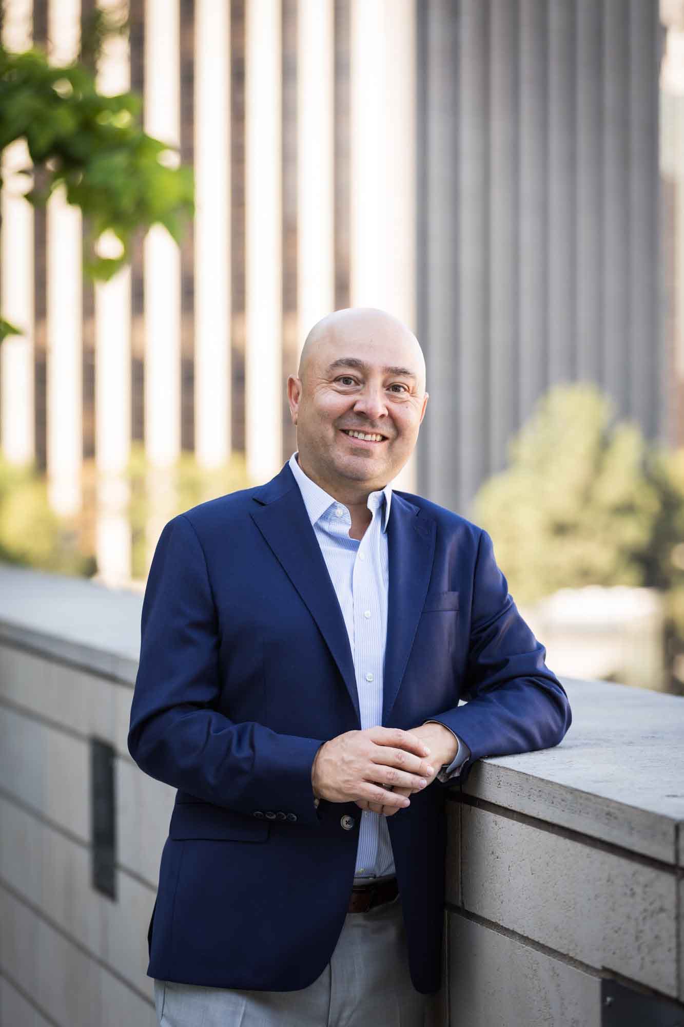 Executive portrait of businessman wearing blue jacket and khaki pants holding hands and leaning against concrete wall for an article on how to prepare for a branding photo shoot