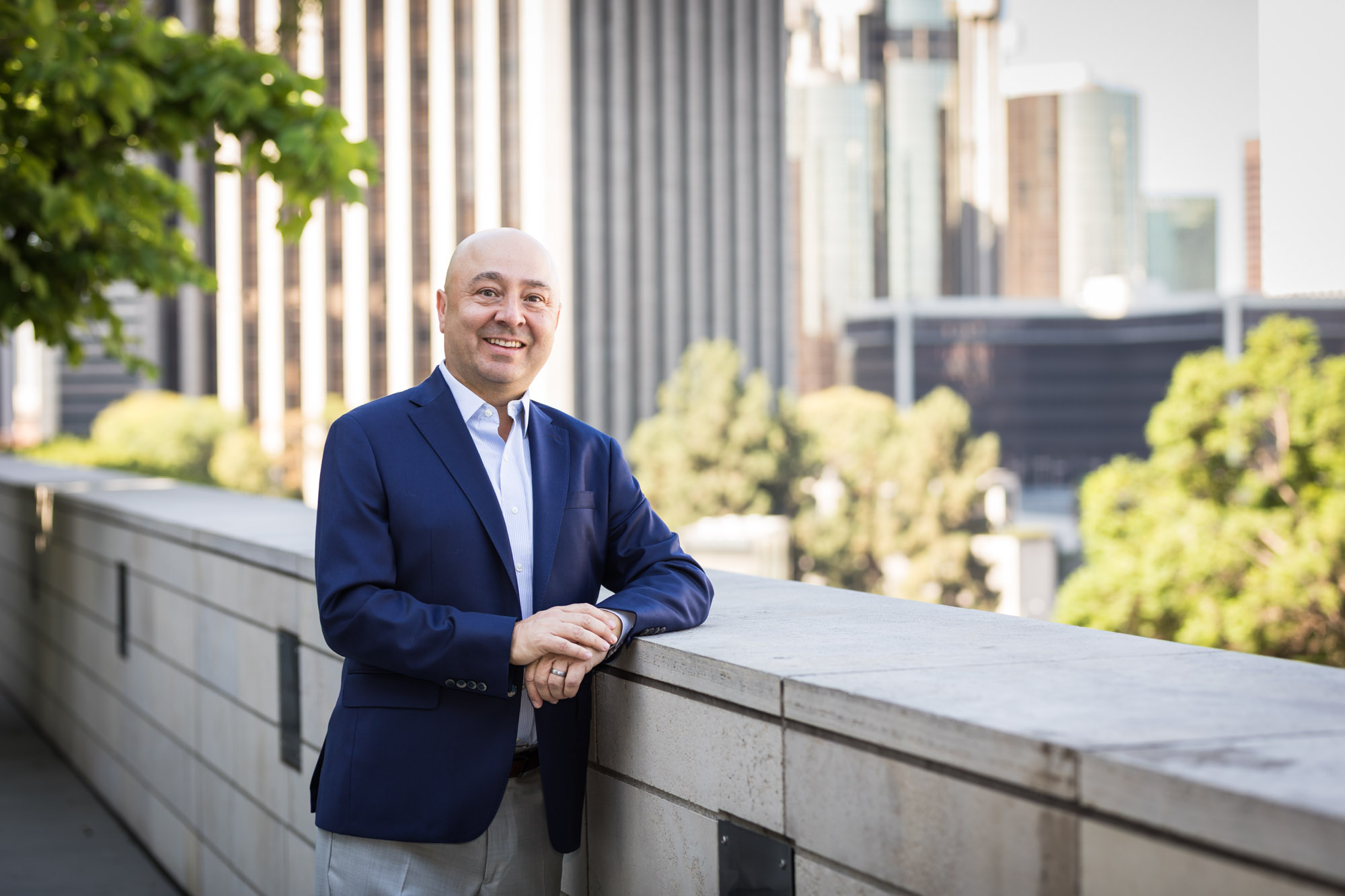 Executive portrait of businessman wearing blue jacket and khaki pants holding hands and leaning against concrete wall for an article on how to prepare for a branding photo shoot