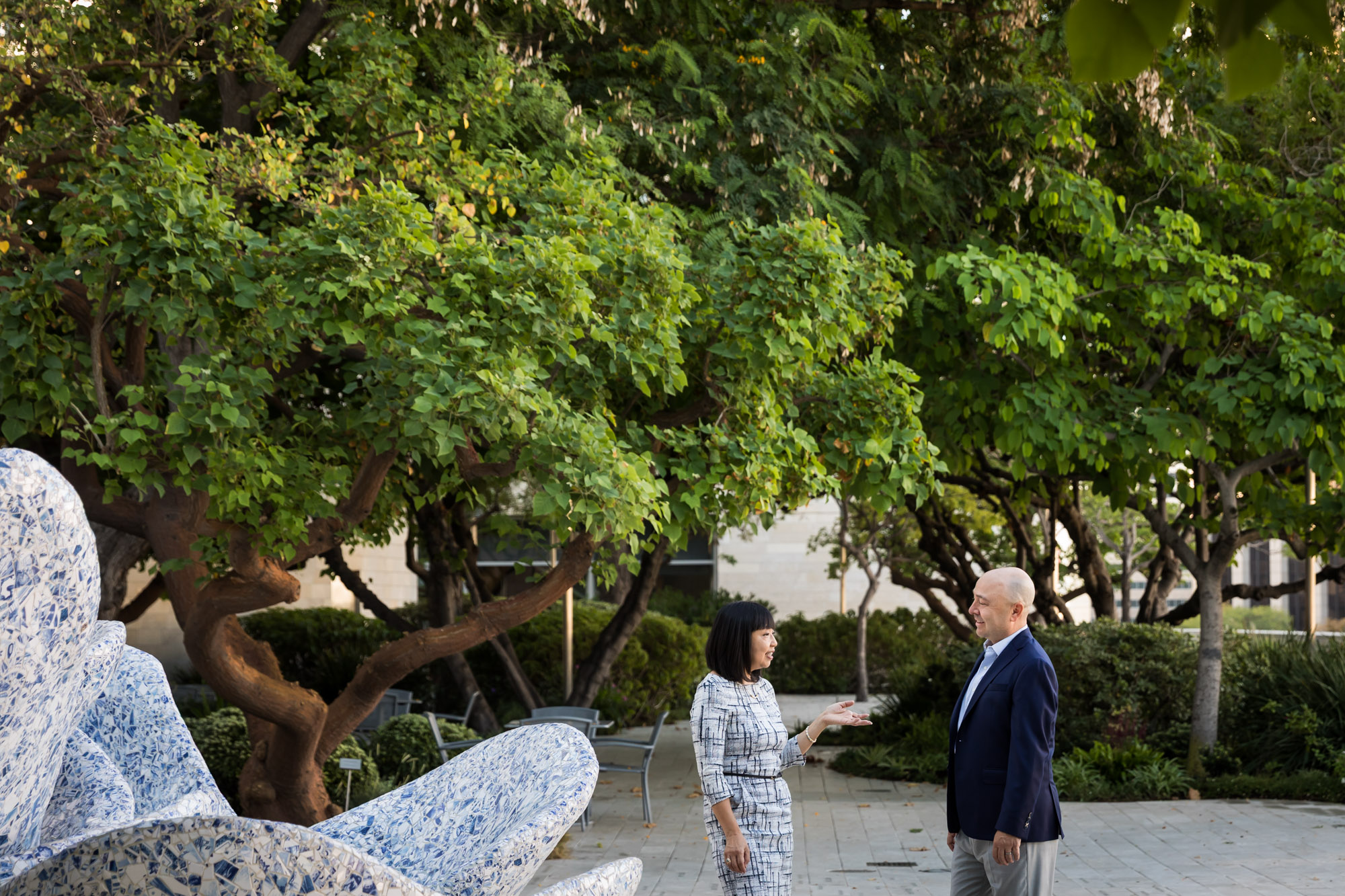 Businessman wearing blue jacket and khaki pants walking and talking with Asian American female colleague wearing dress in Blue Ribbon Garden for an article on how to prepare for a branding photo shoot