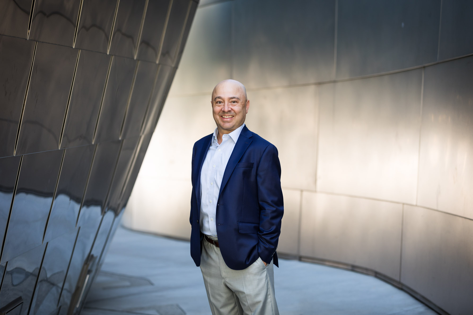 Executive portrait of businessman wearing blue jacket and khaki pants standing with hands in pockets in front of metal wall for an article on how to prepare for a branding photo shoot